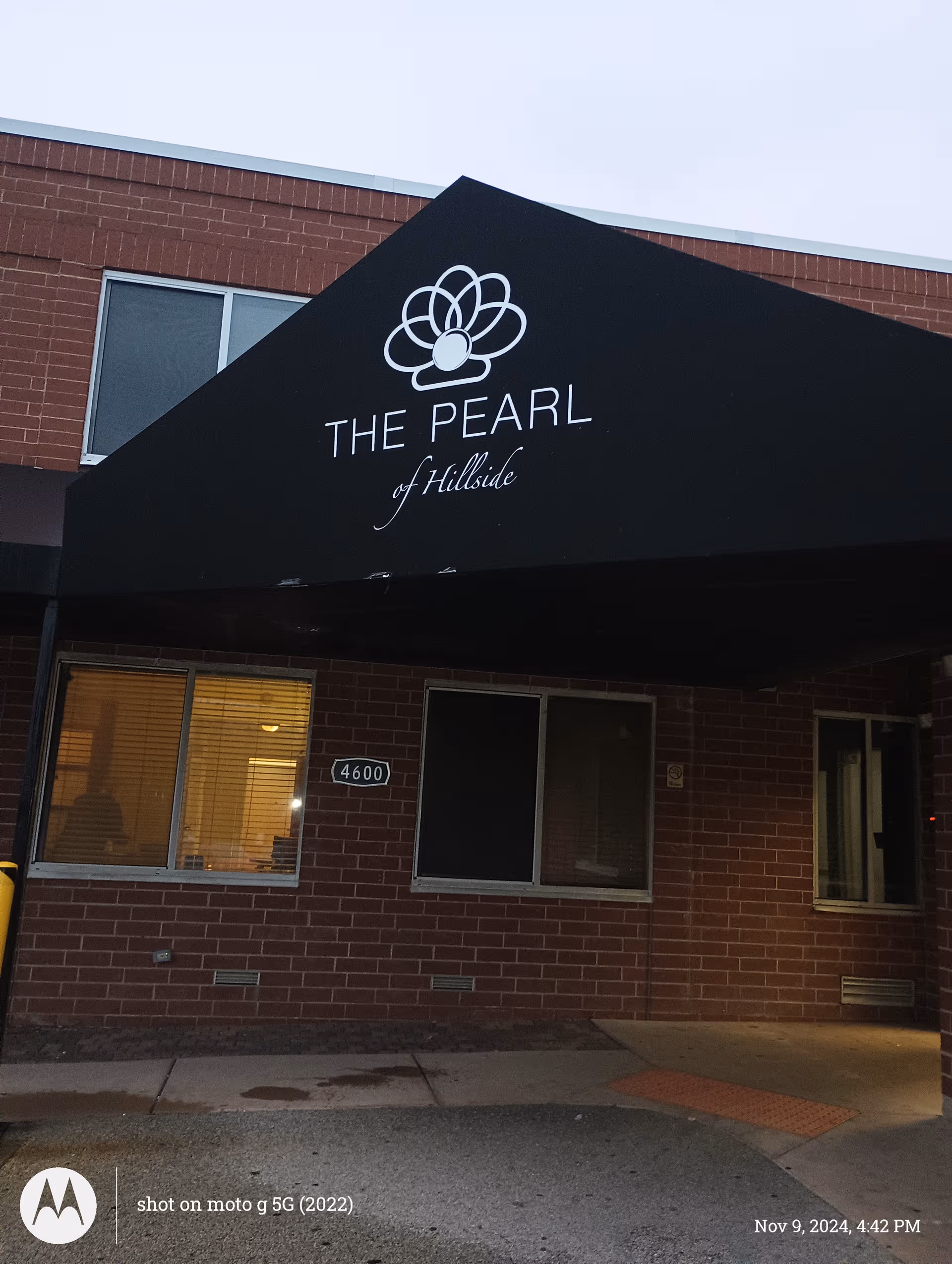 Exterior view of The Pearl of Hillside facility entrance with brick facade and sign.