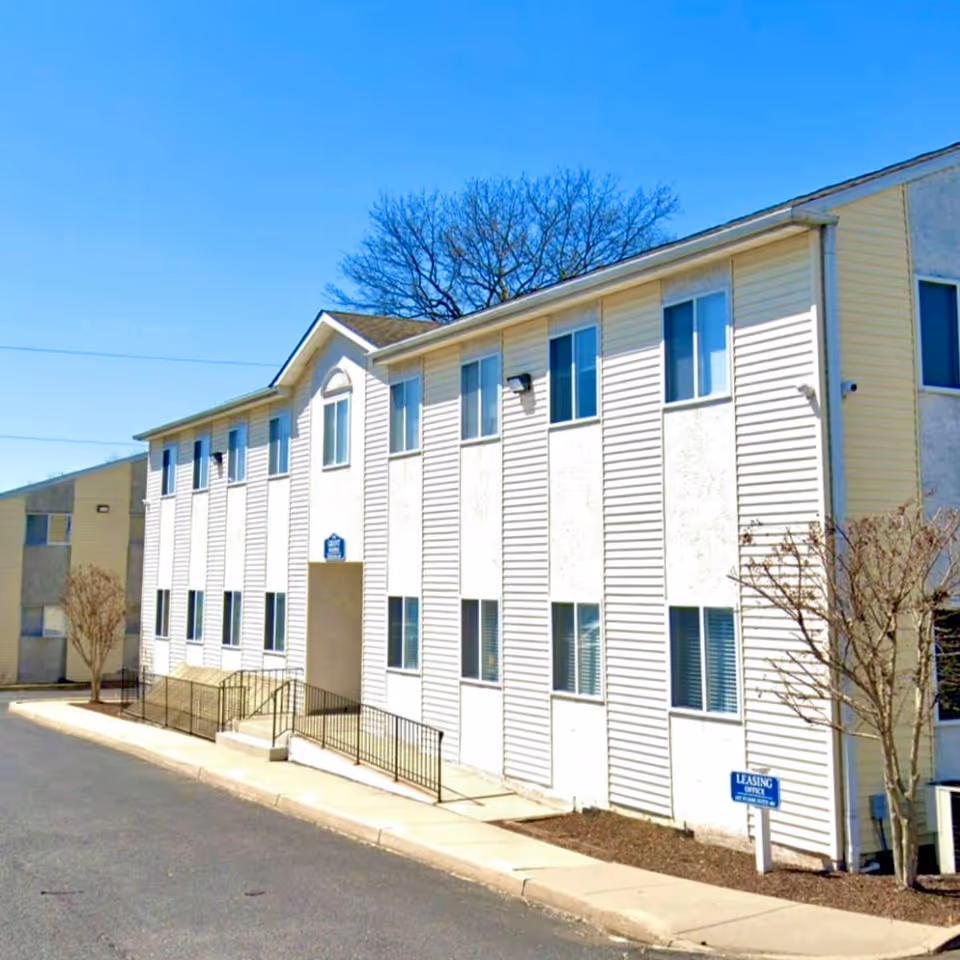 White multi-story senior living facility exterior with ramp and leafless trees.