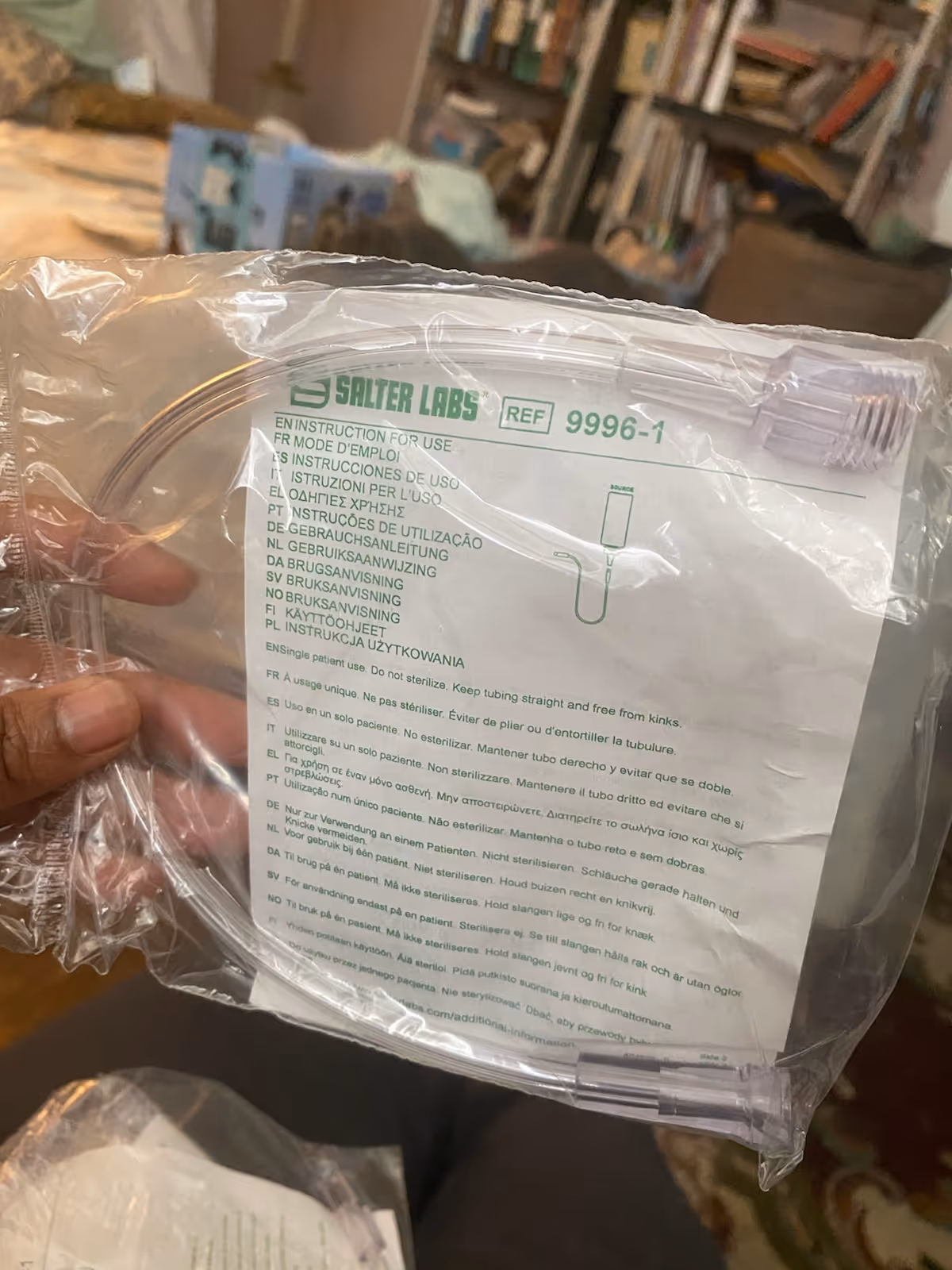 Hand holds clear bag labeled Salter Labs with instructions in a cozy, book-filled room.