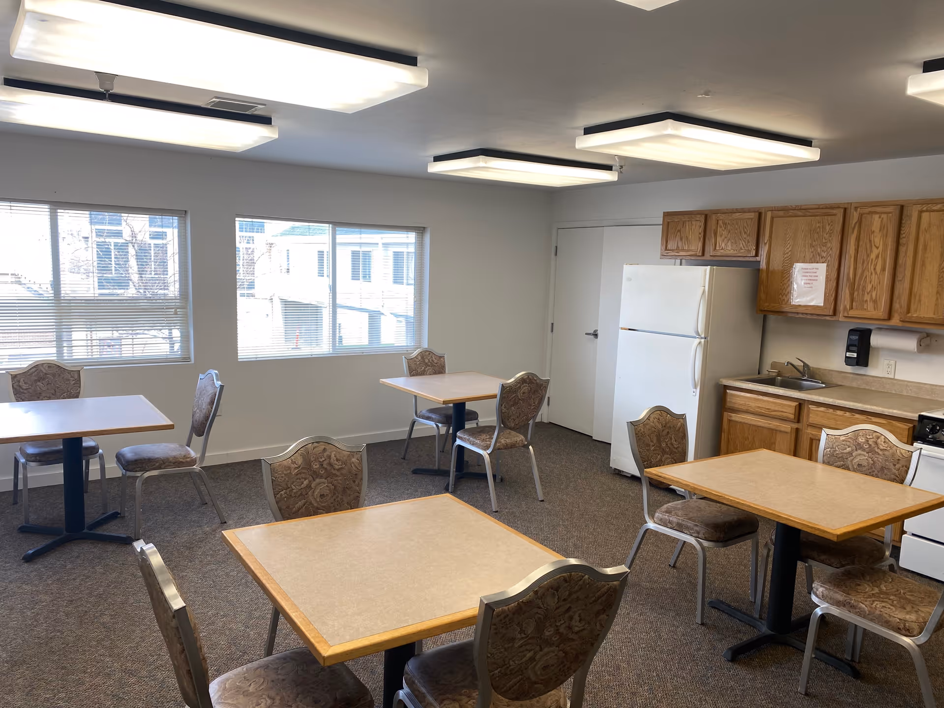 Communal dining area with several tables and chairs, plus a kitchenette along the wall.