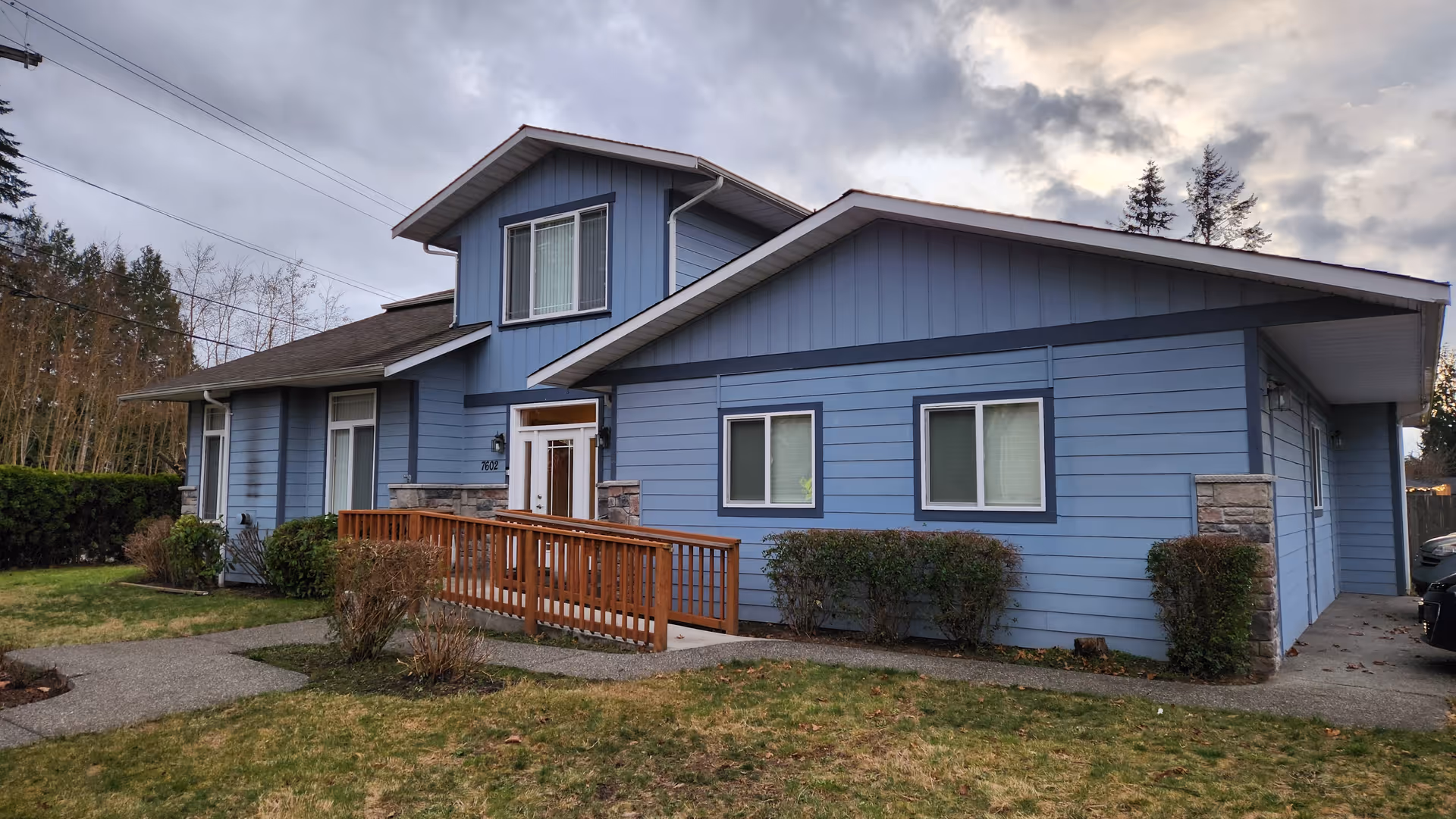 Blue multi-section adult family home exterior with ramp to entrance and shrubs.