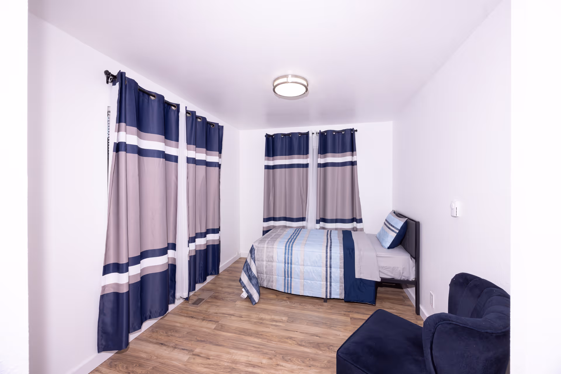 A tidy bedroom with a bed, blue striped bedding, and curtains.