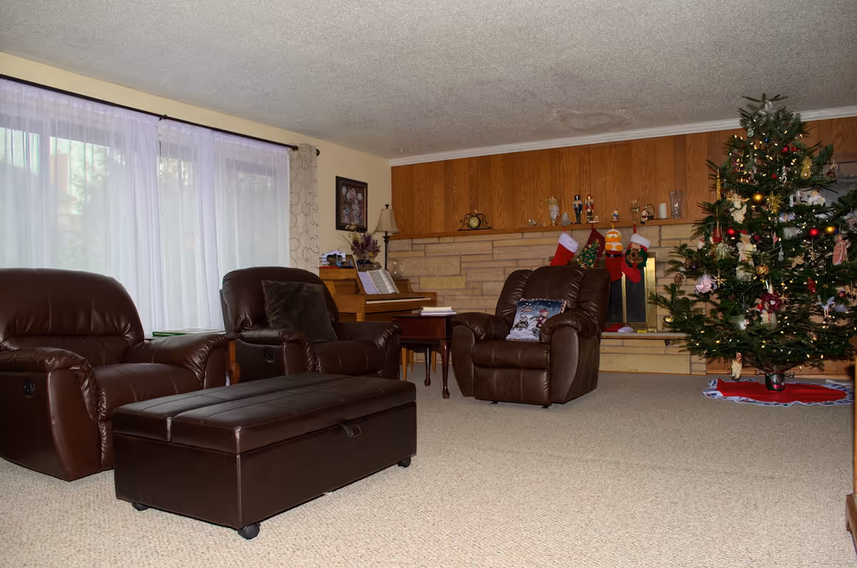 Cozy living room with brown leather seating, a Christmas tree, stockings, and a piano.
