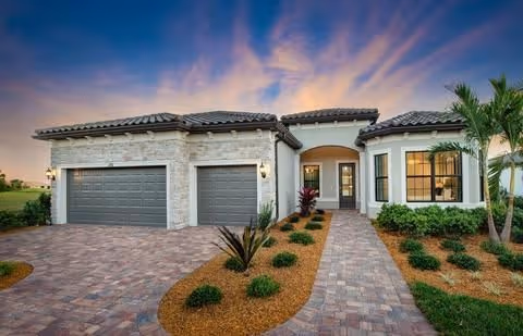 Front exterior of a single-story Mediterranean-style home with a three-car garage, paved driveway, and landscaped front yard at sunset.