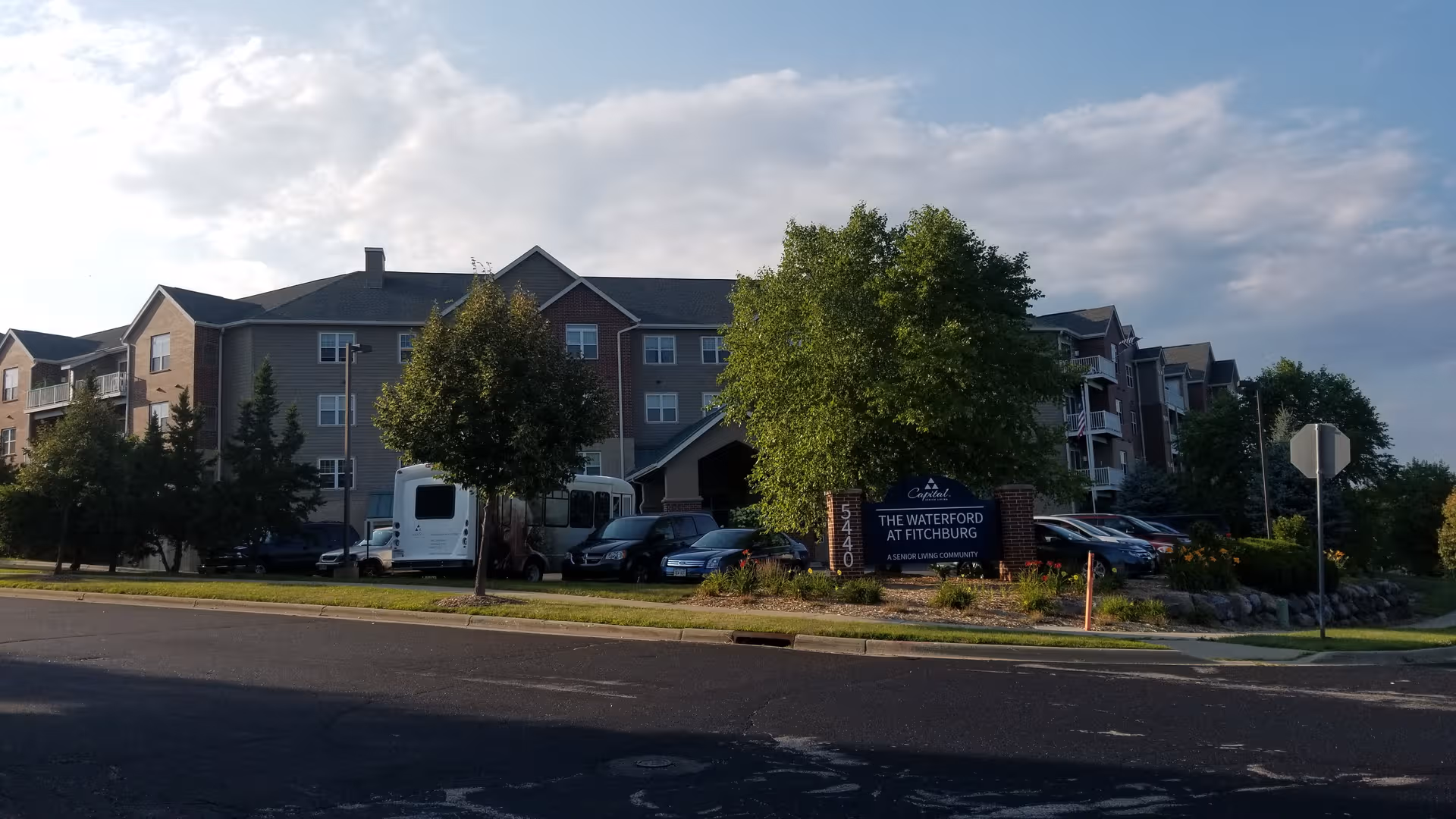 Exterior view of The Waterford at Fitchburg building with trees and parked cars.