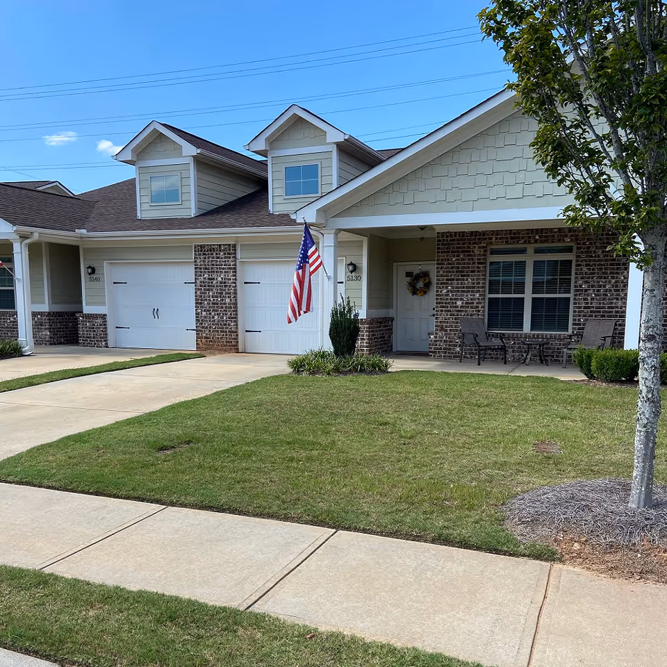 Residential-style facility front with two garage bays, porch seating, and an American flag.
