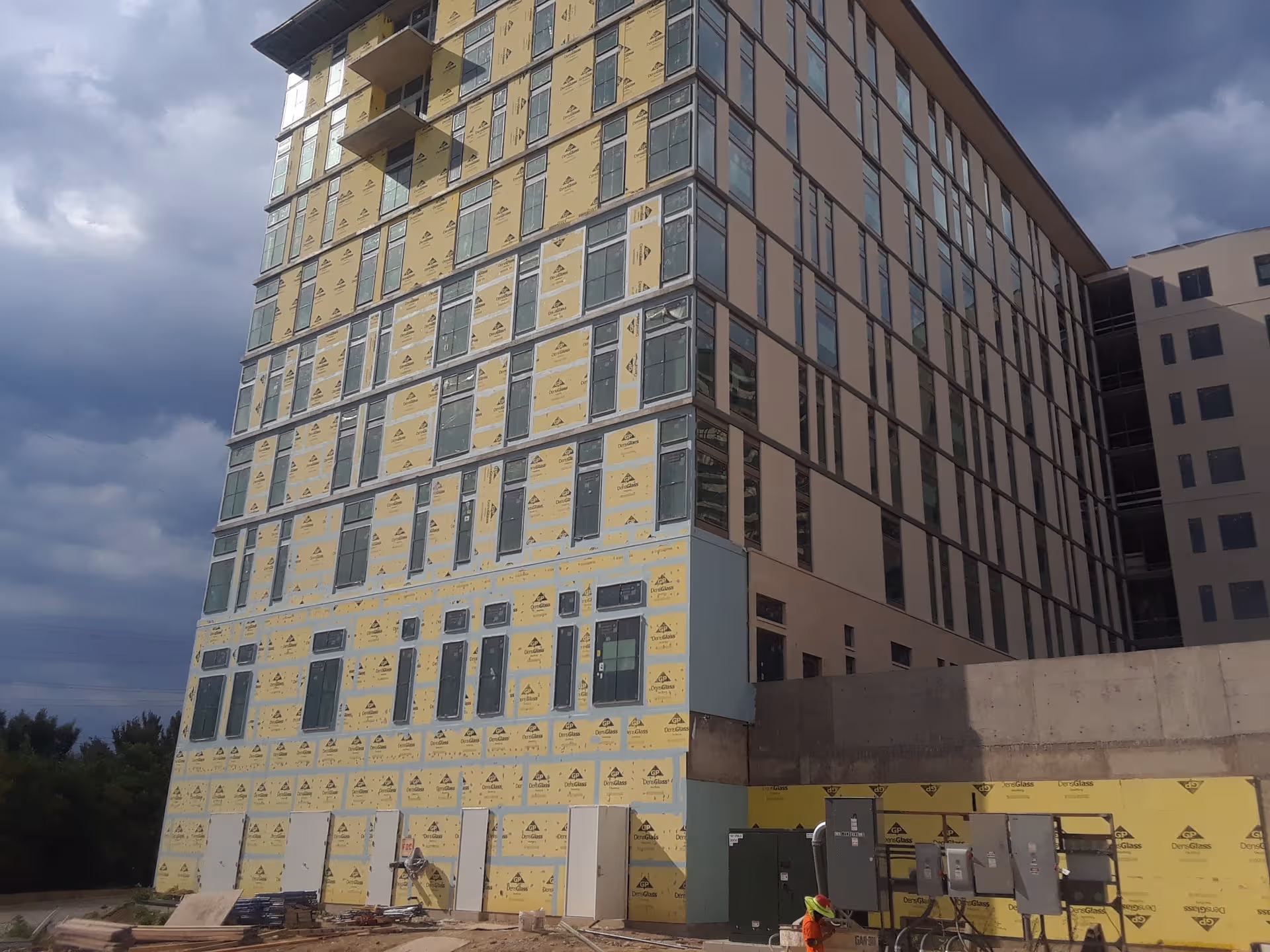 Tall multi-story building under construction with yellow insulation panels on facade.