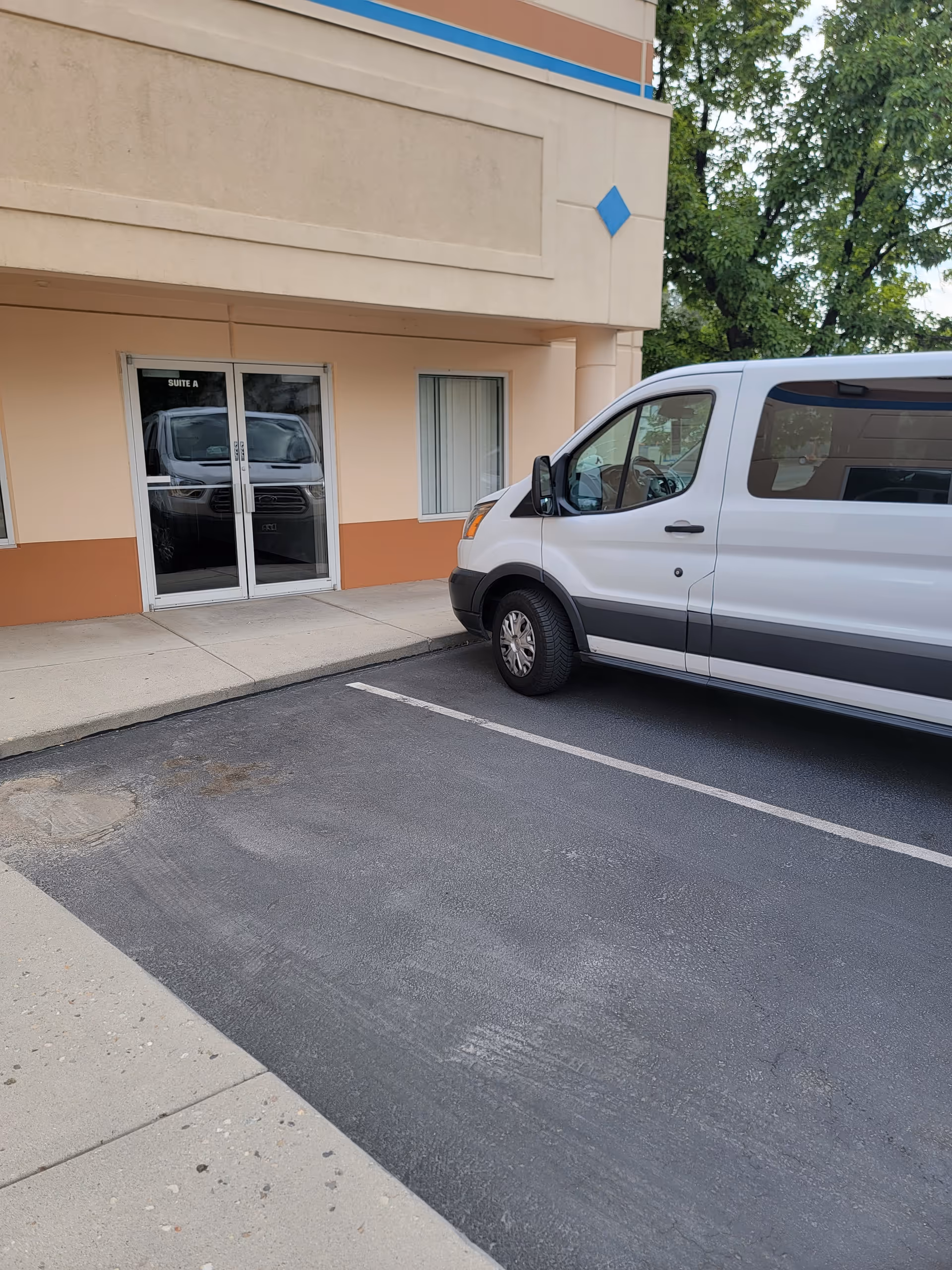 Beige building exterior with glass entrance doors and a white van parked in front.