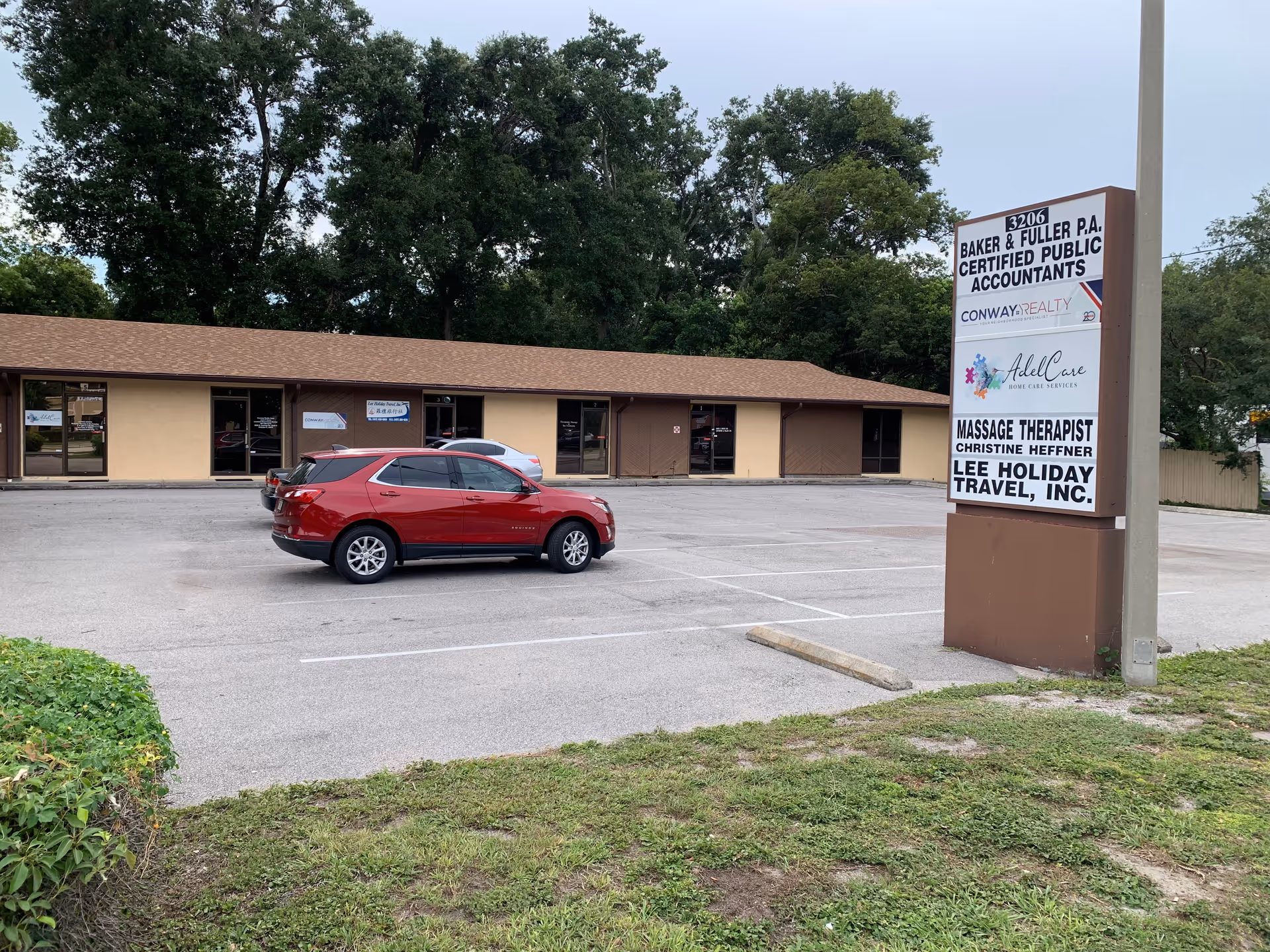 Parking lot in front of a beige commercial strip, red SUV parked, tall sign.