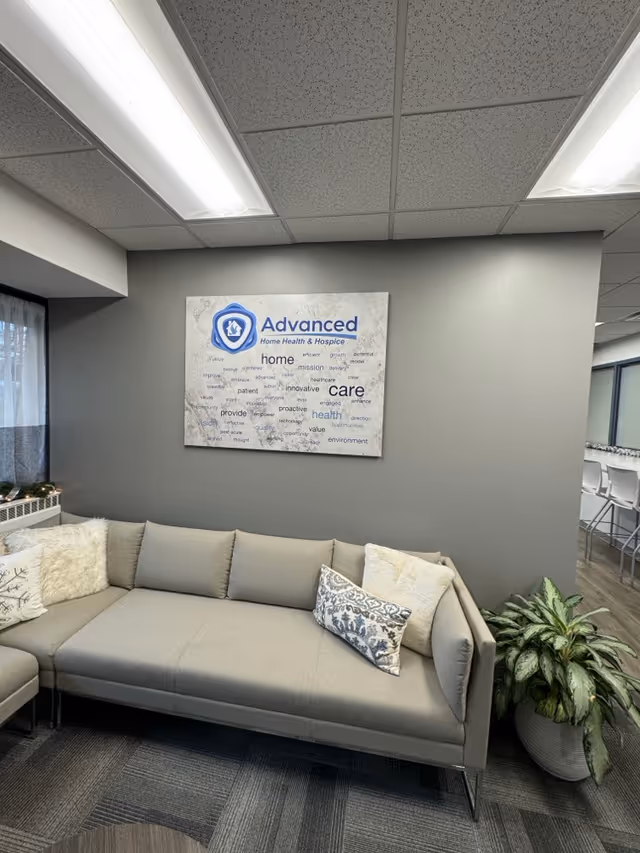 Gray sectional sofa in a lounge area with a wall sign displaying Advanced Home Health.