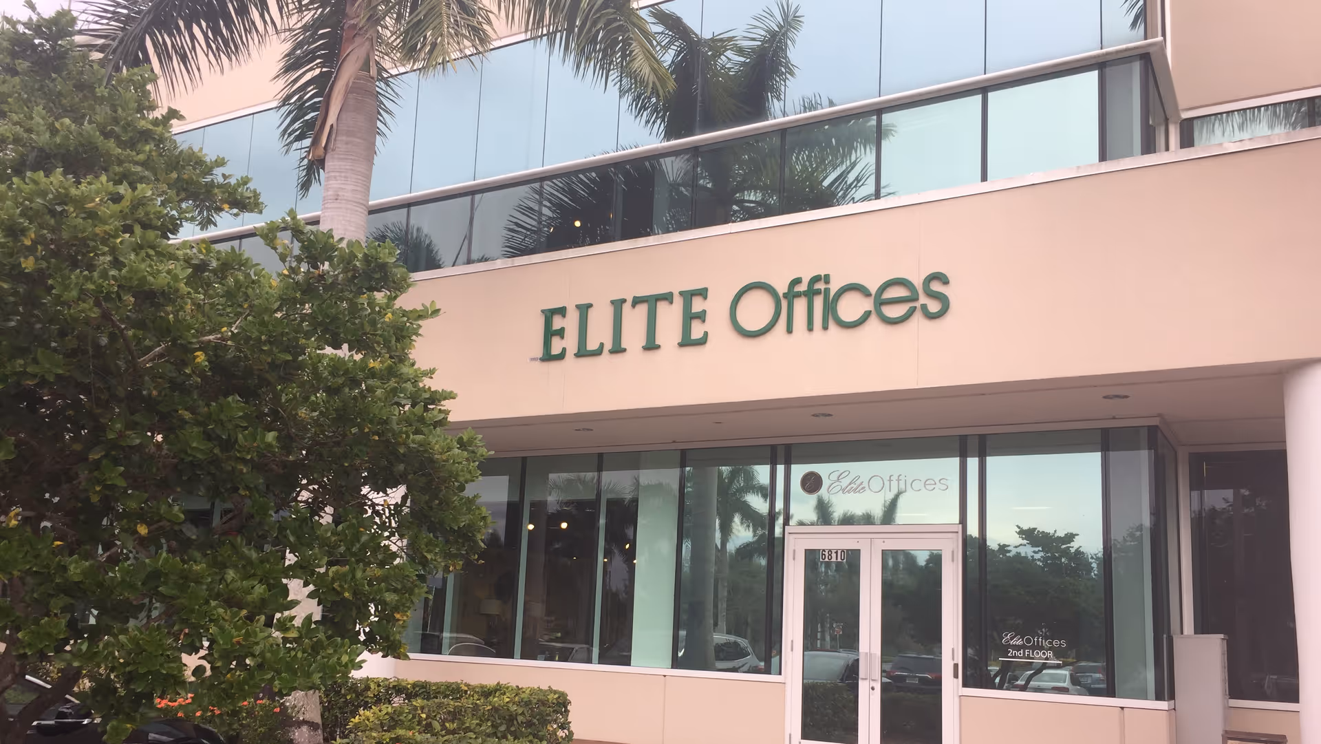 Front exterior of a building with Elite Offices sign and glass doors, flanked by palm trees.