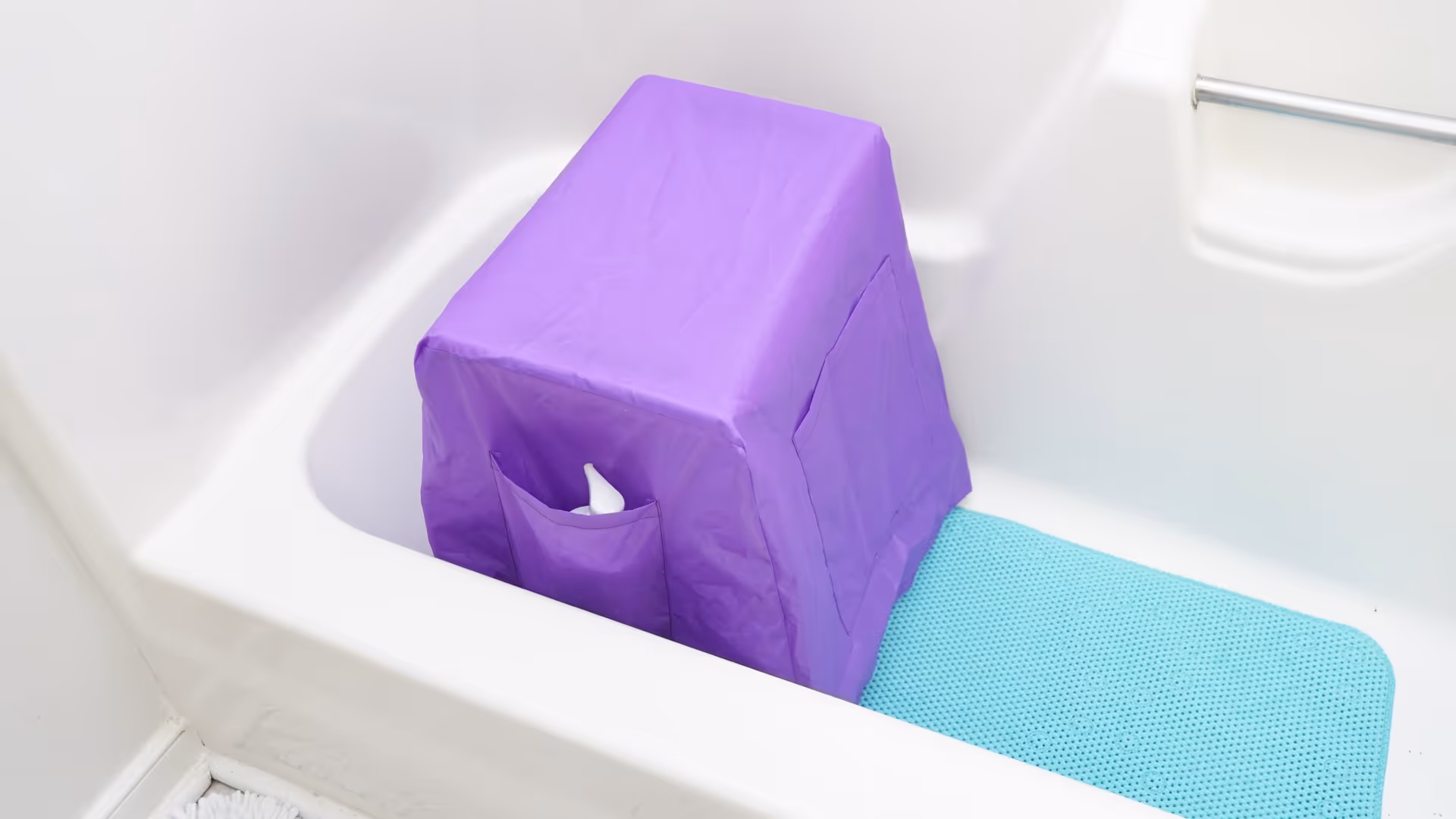 Purple fabric-covered object inside a white bathtub, beside a teal non-slip mat.