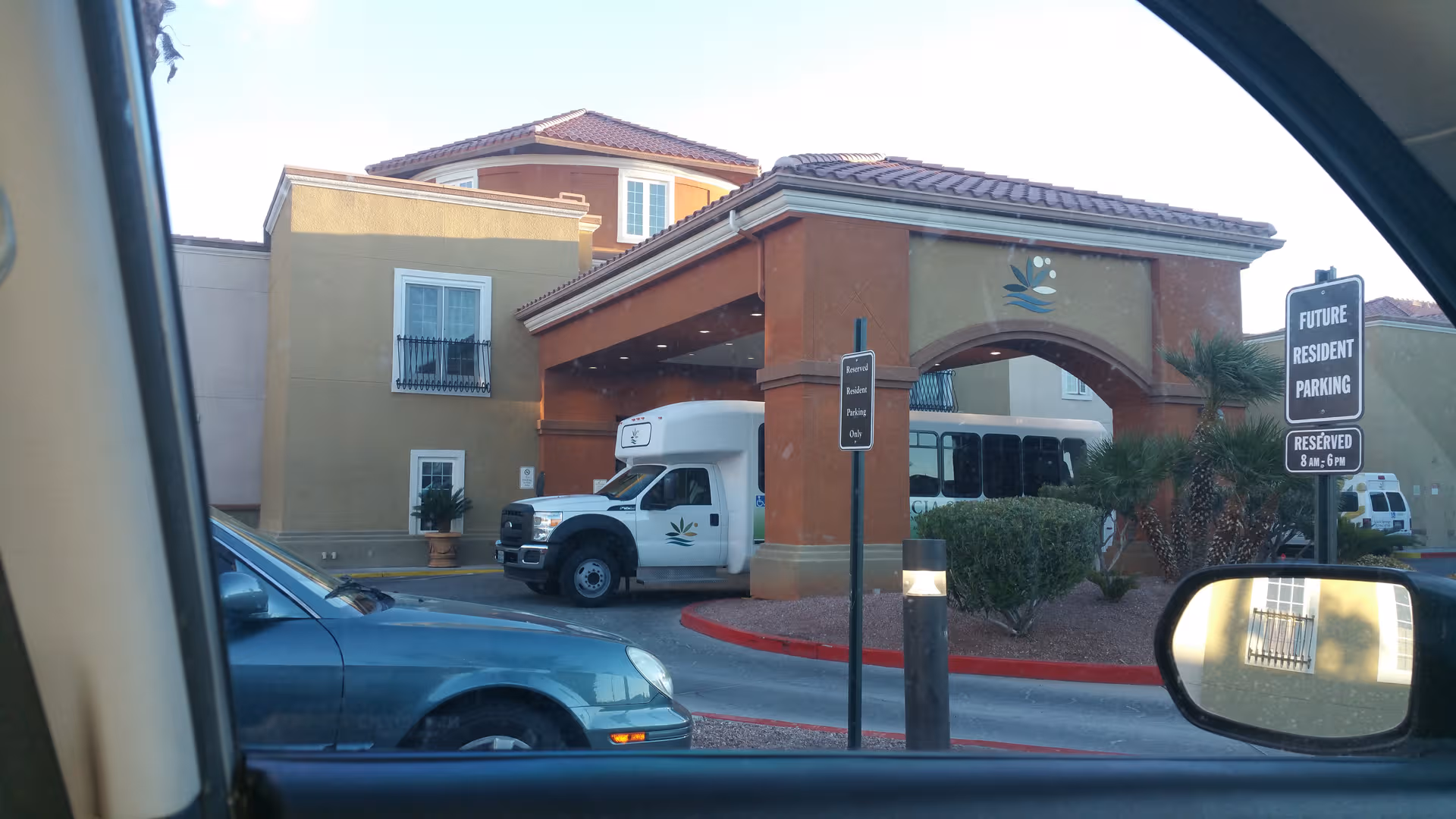 Exterior view of Acacia Springs senior living entrance with a bus and parked cars.