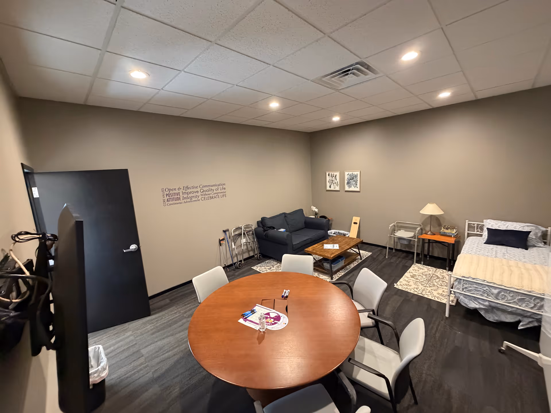Interior common area with round table, sofa, and a bed visible along the wall.