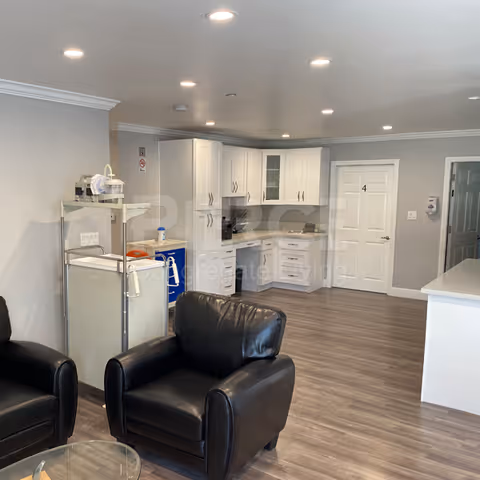 Modern kitchenette with white cabinets, appliances, and black leather seating in a common area.