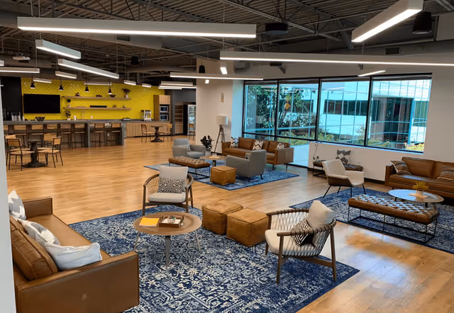 Open lounge area with couches, chairs, tables, and blue rugs in a bright facility.