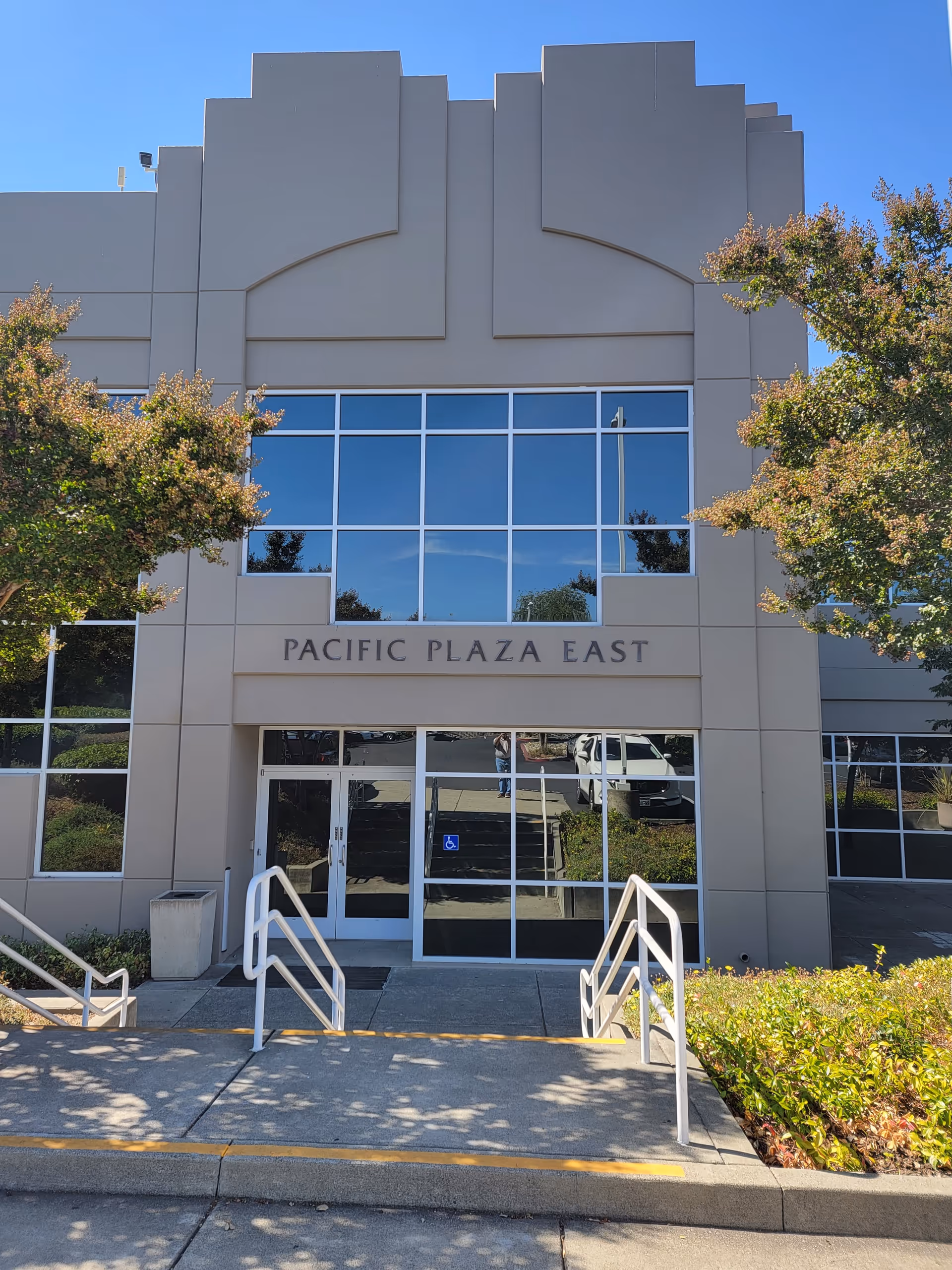 Front of a beige building with large glass doors and Pacific Plaza East sign.