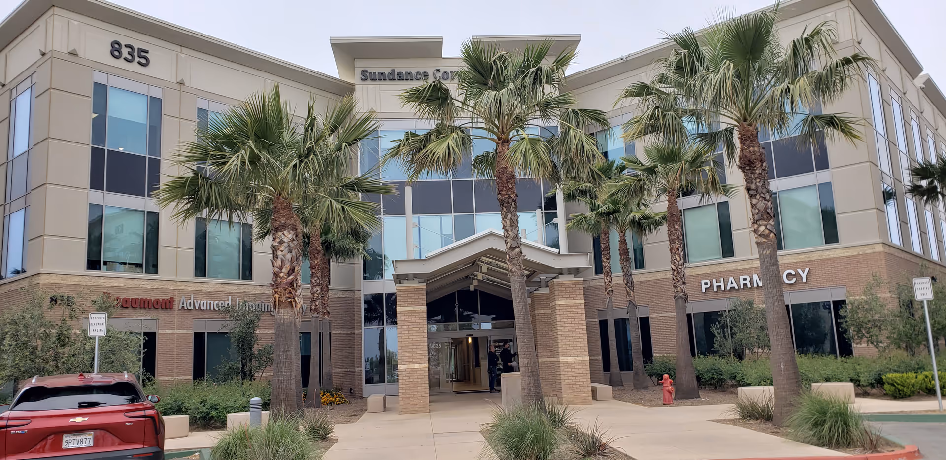 Beige modern building with palm trees and a glass entrance.