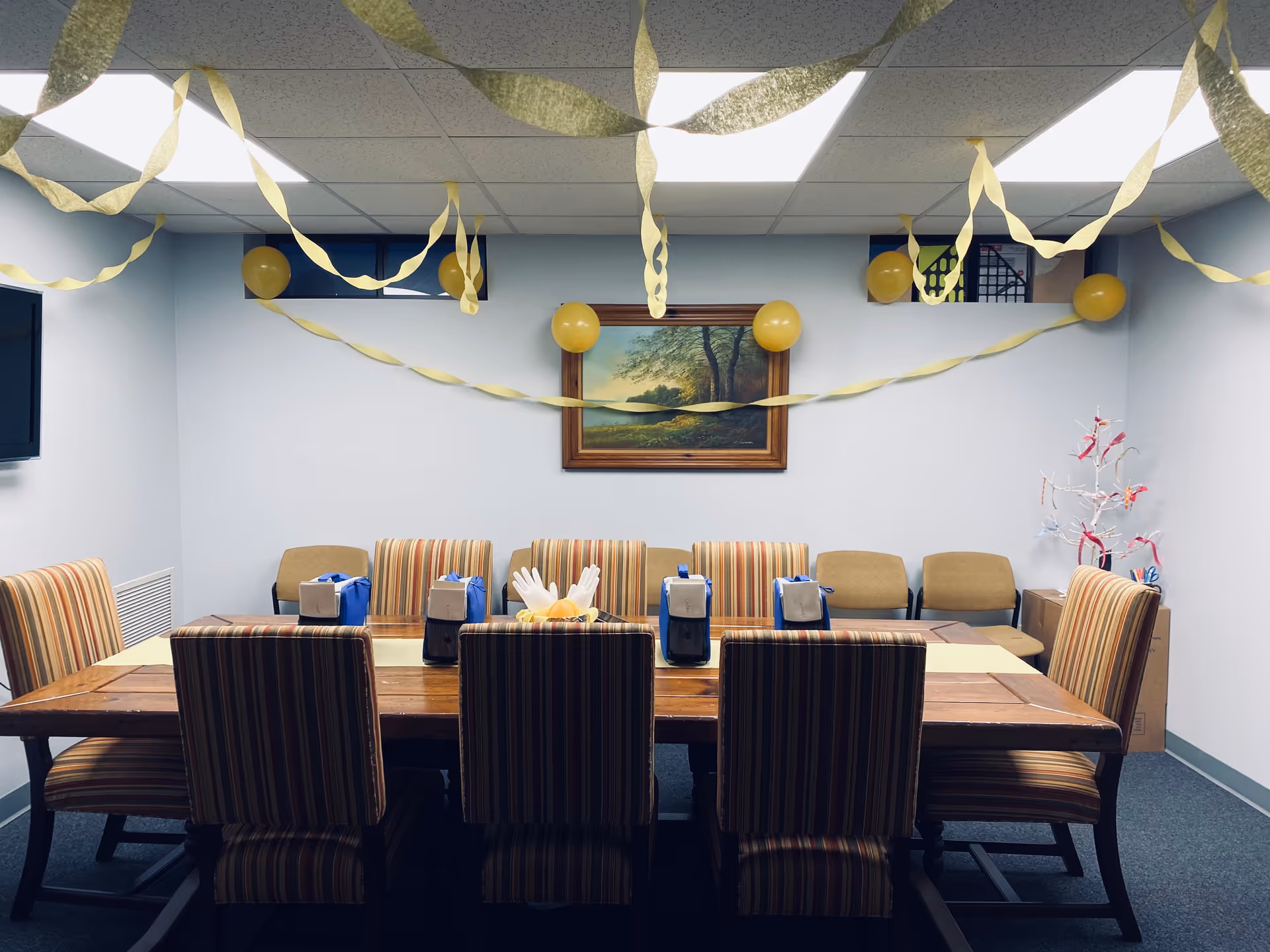 A decorated dining room with a long table, striped chairs, gift bags, balloons, and streamers.