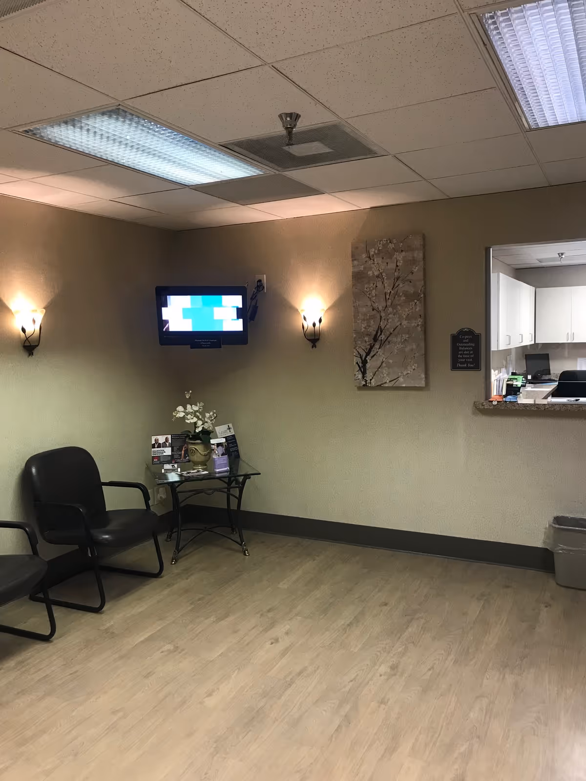 A small waiting area with two black chairs, a glass table, a TV, and wall sconces.