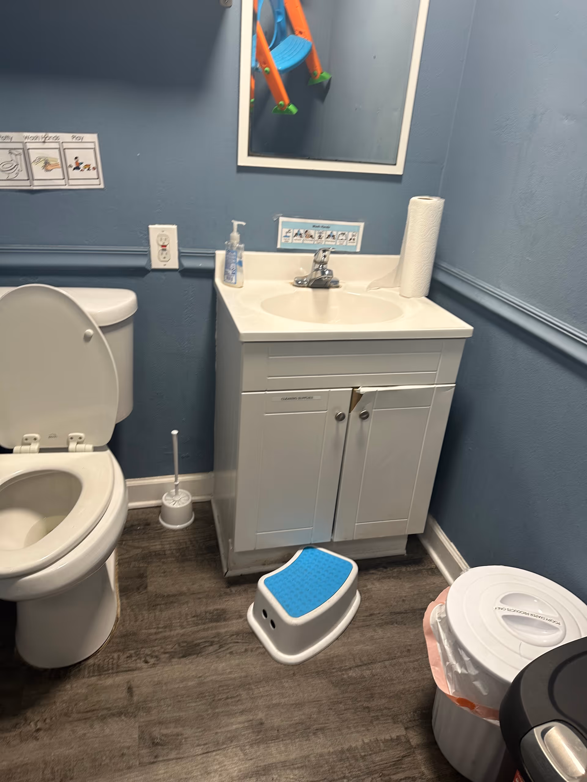 Small bathroom with toilet, sink vanity, mirror, and a blue step stool.