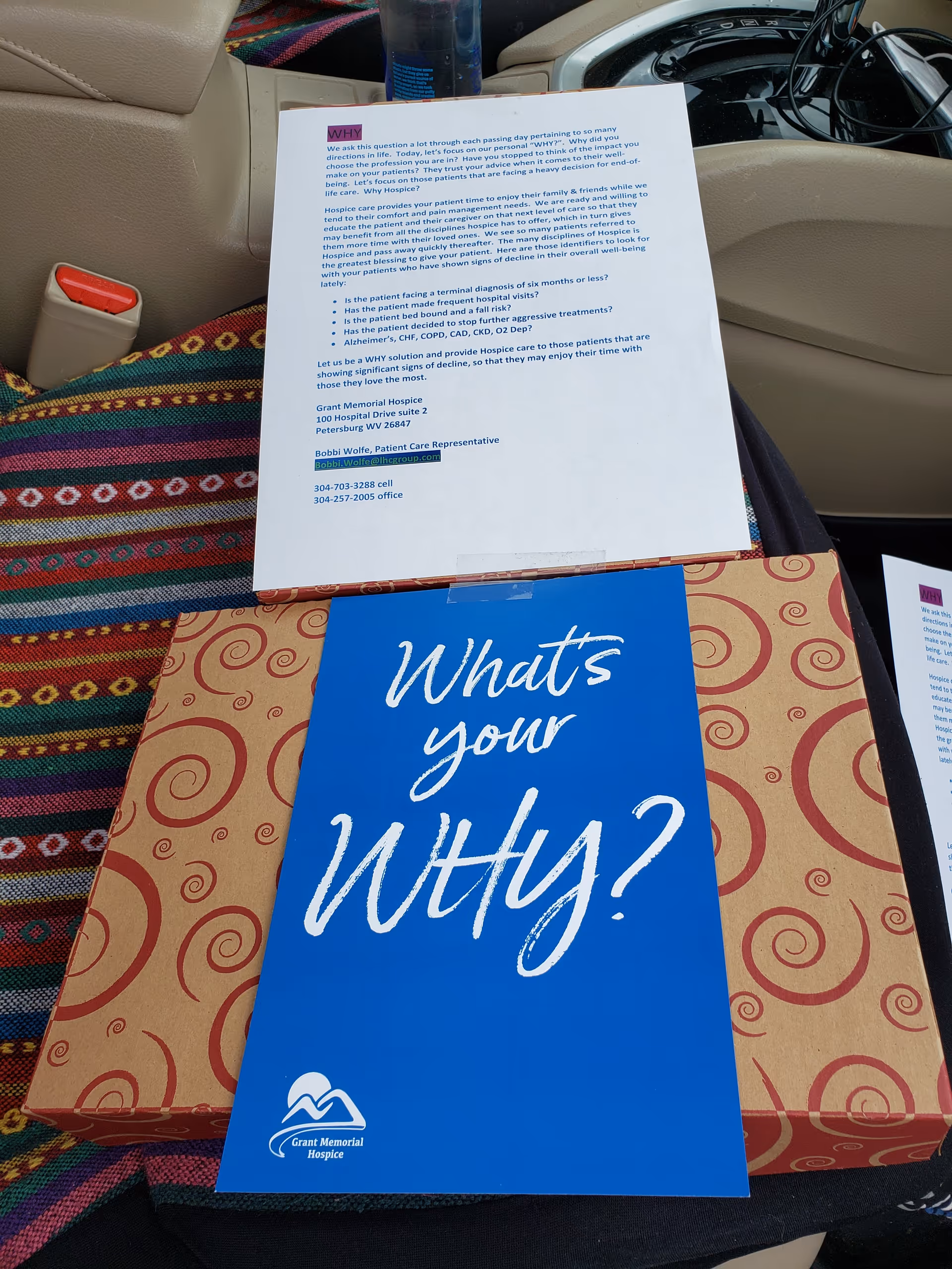 Inside a car, promotional papers and a blue 'What's your Why?' brochure lie on the seats.