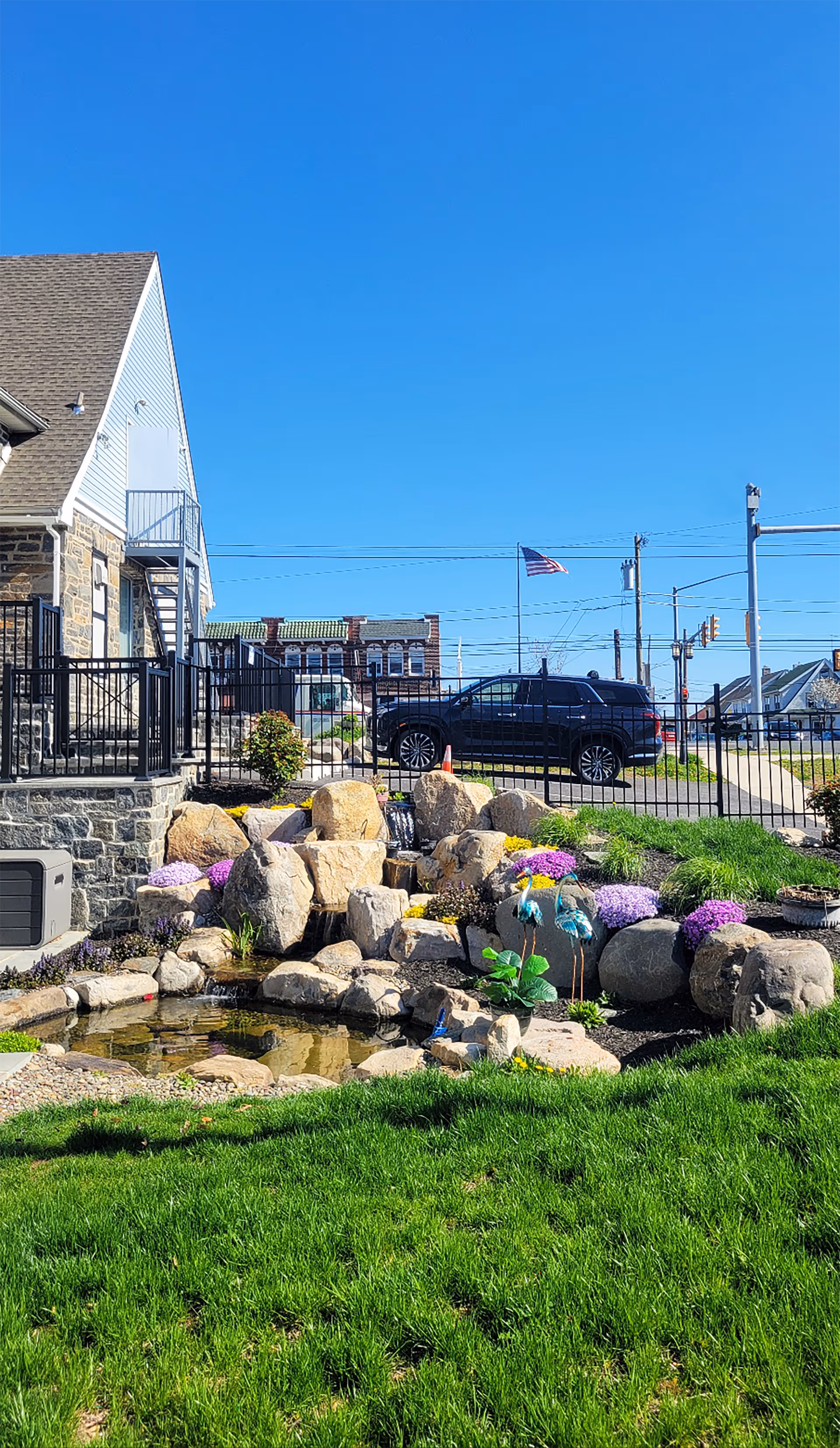 Exterior view of HomePlus Care with landscaped rocks, pond, and a parked SUV.