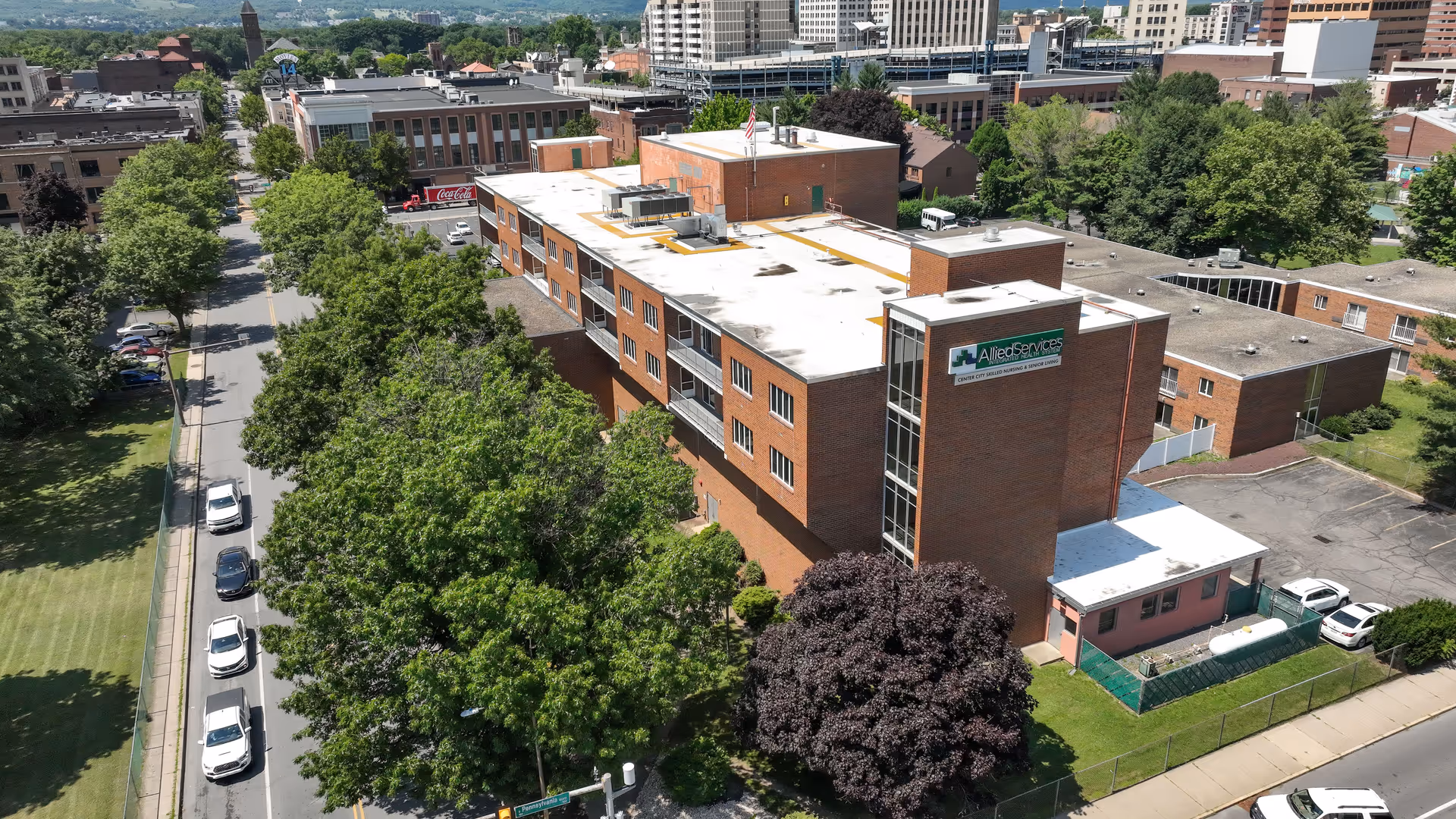 Aerial view of St. Luke's Villa, a brick senior living facility, with trees and city skyline.