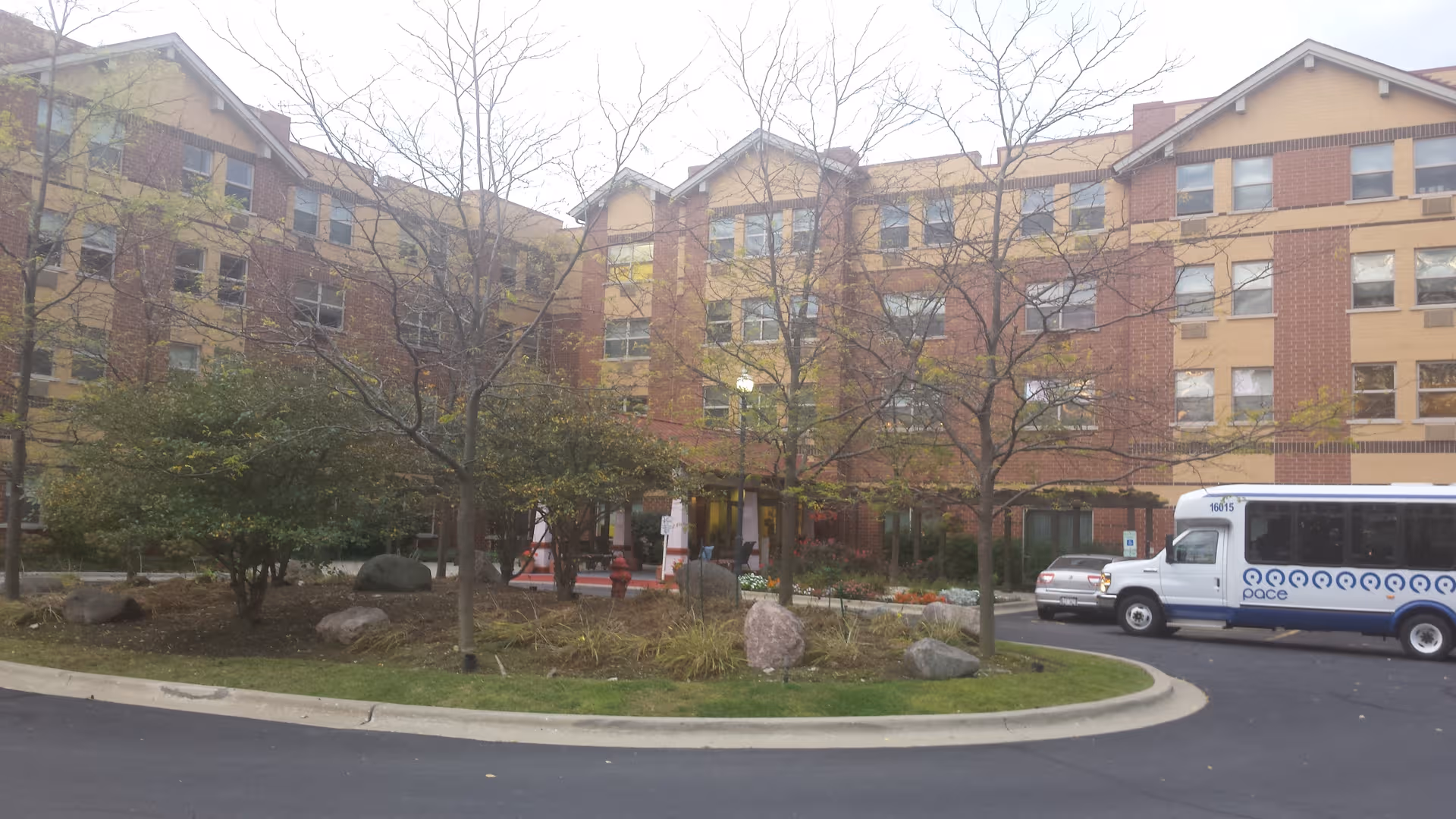Brick senior residence building with trees, a circular driveway, and a parked bus.
