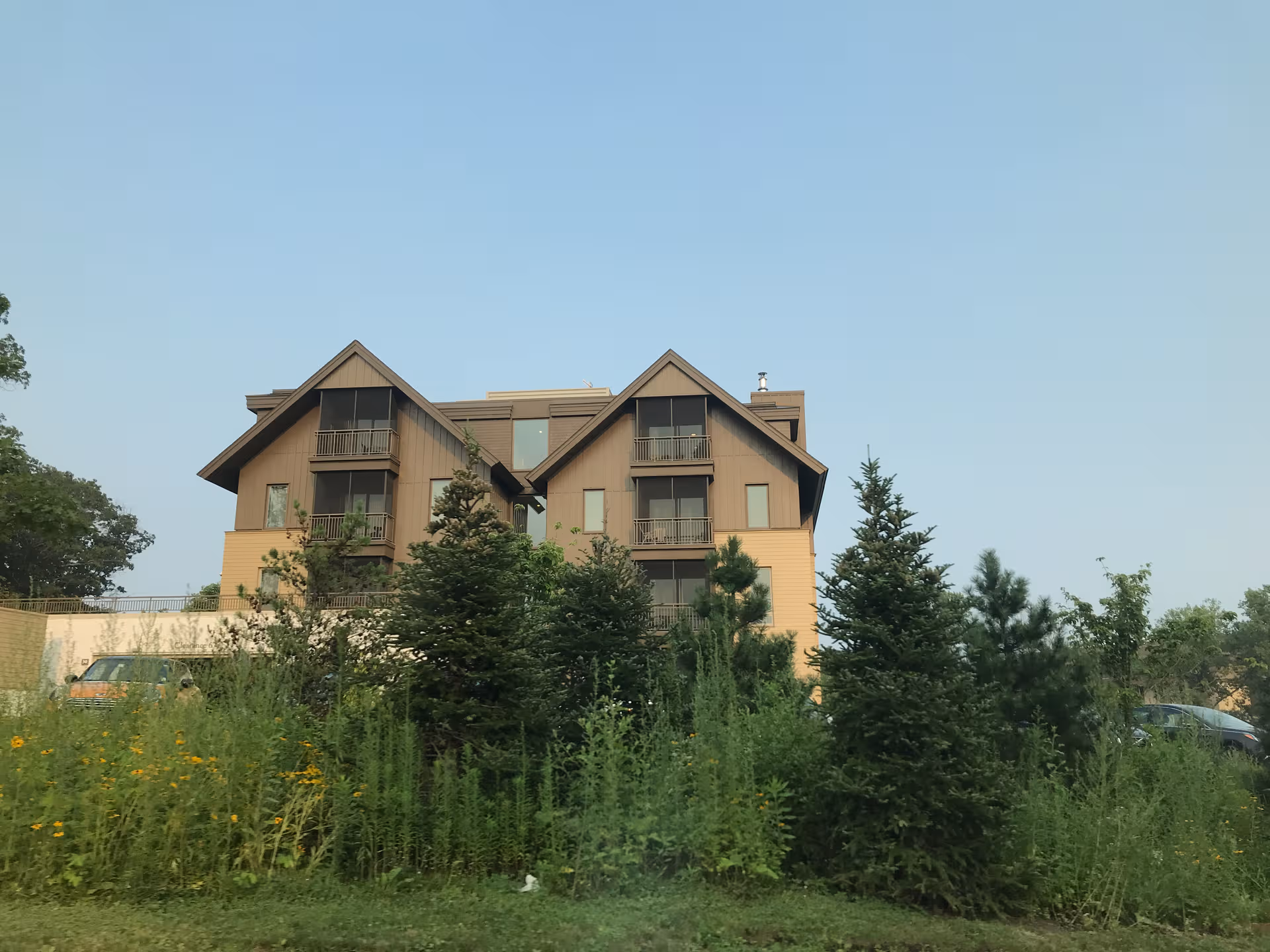 A multi-story wooden building with balconies sits amid tall grasses and trees.