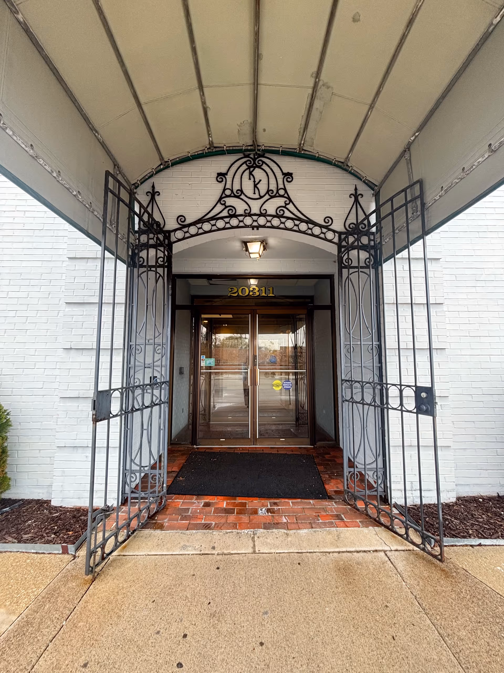 Front entrance with ornate iron gate and glass doors under curved canopy.