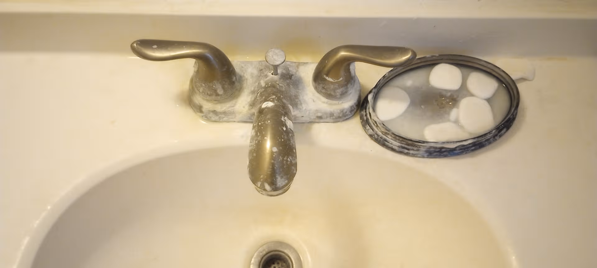 Close-up of a bathroom sink faucet with a dish of white stones nearby.