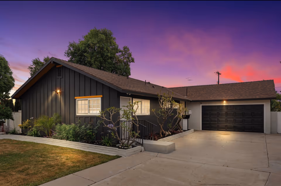 Exterior of a single-story senior living facility with a dark facade and two-car garage at dusk.