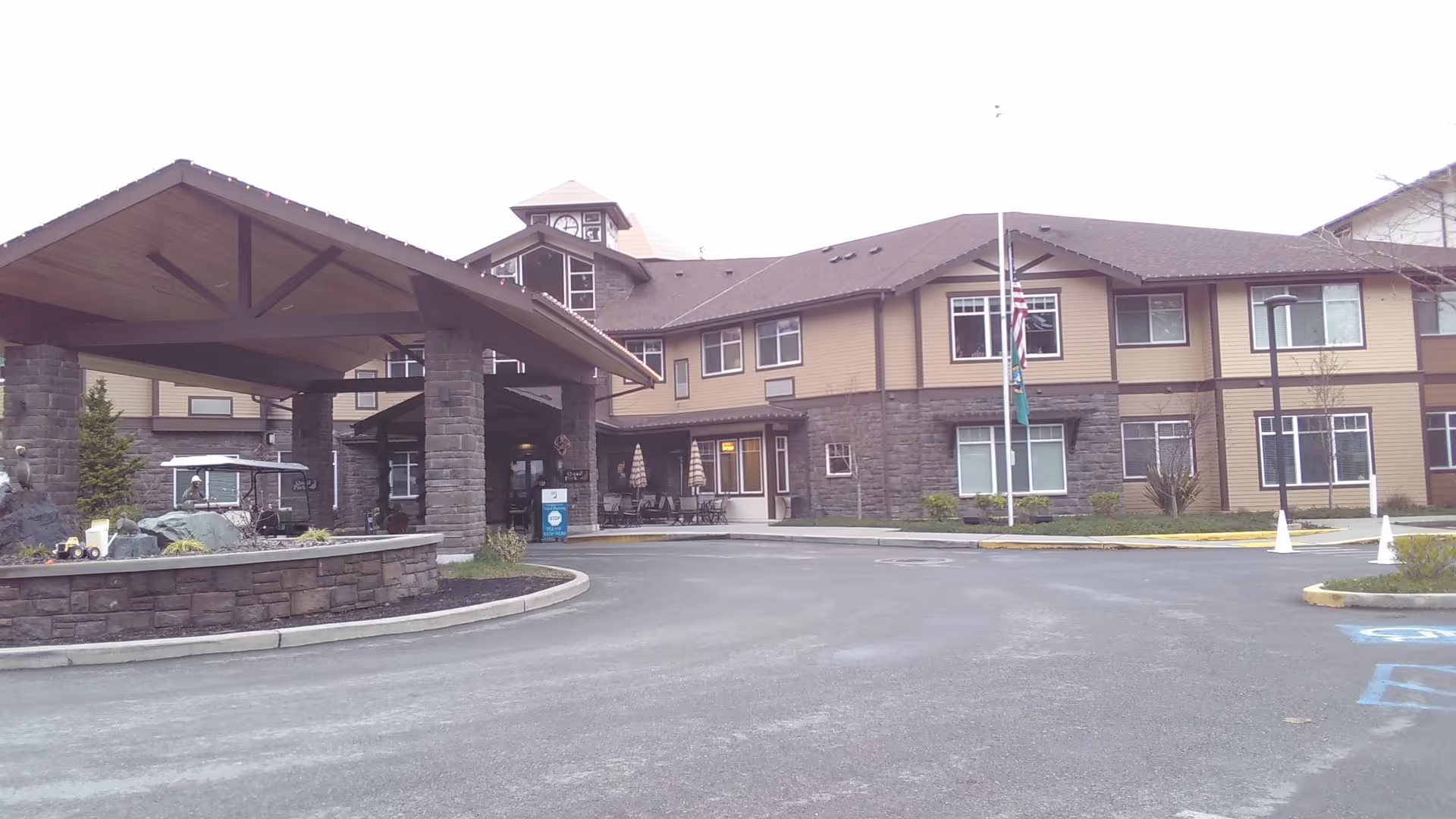 Exterior view of Quail Park of Lynnwood with covered entrance, driveway, and flagpole.