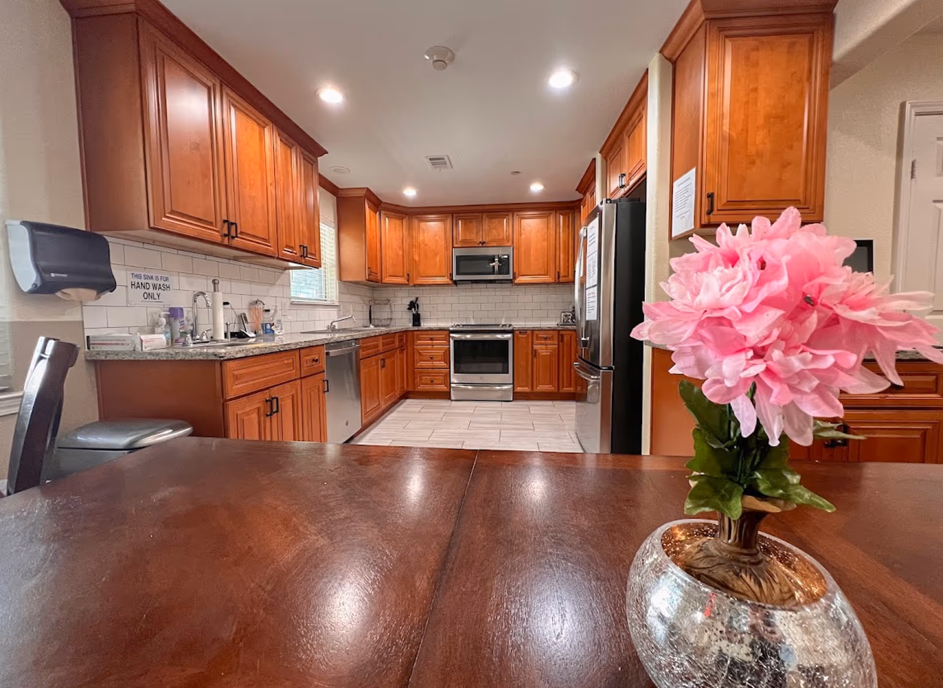 A spacious kitchen with wooden cabinets, stainless steel appliances, and a flower centerpiece on a table.