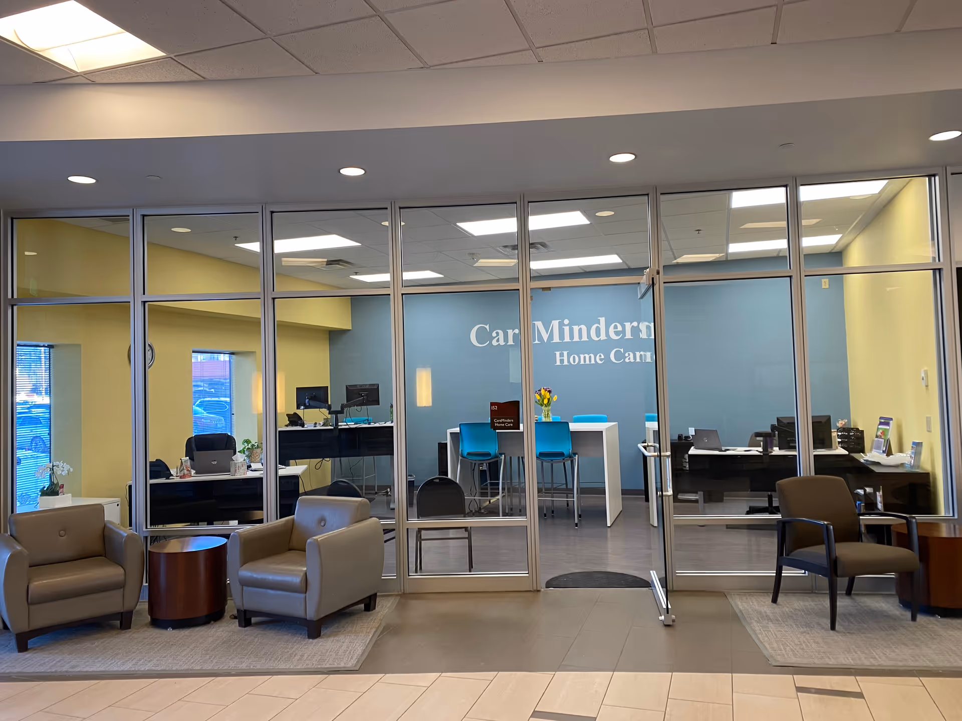 Glass-walled lobby with blue wall, desks, and seating in CareMinders Home Care.