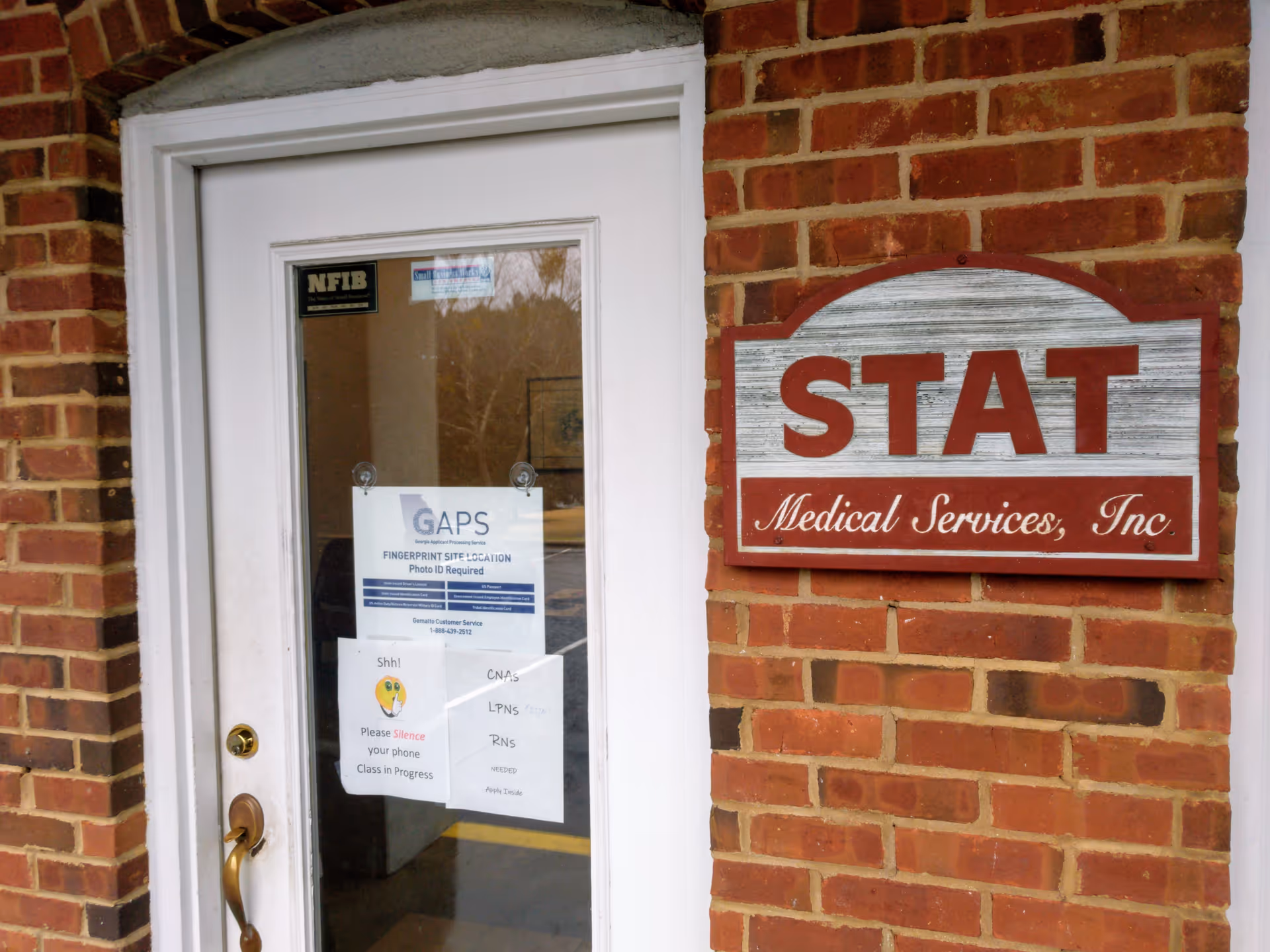 Brick exterior doorway with a STAT Medical Services sign beside a white door.