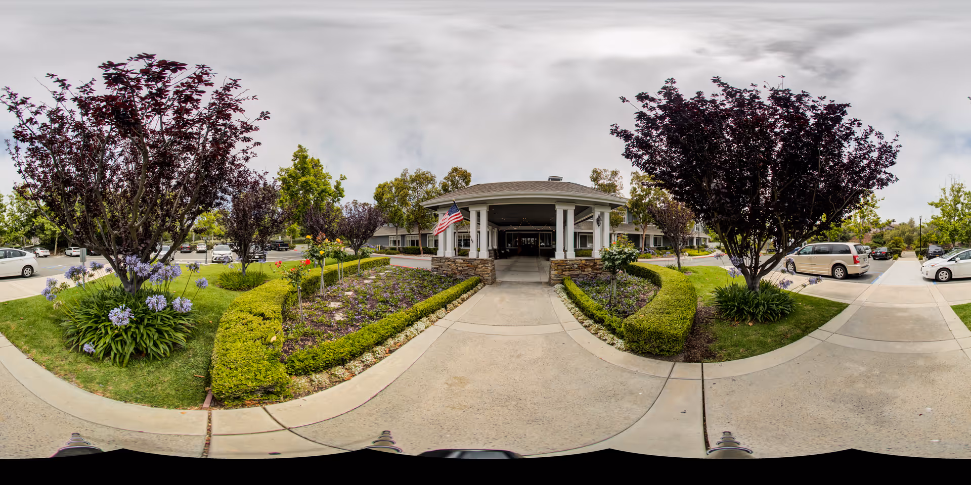 Panoramic view of Aegis Living Laguna Niguel entrance with landscaped walkway and parked cars.