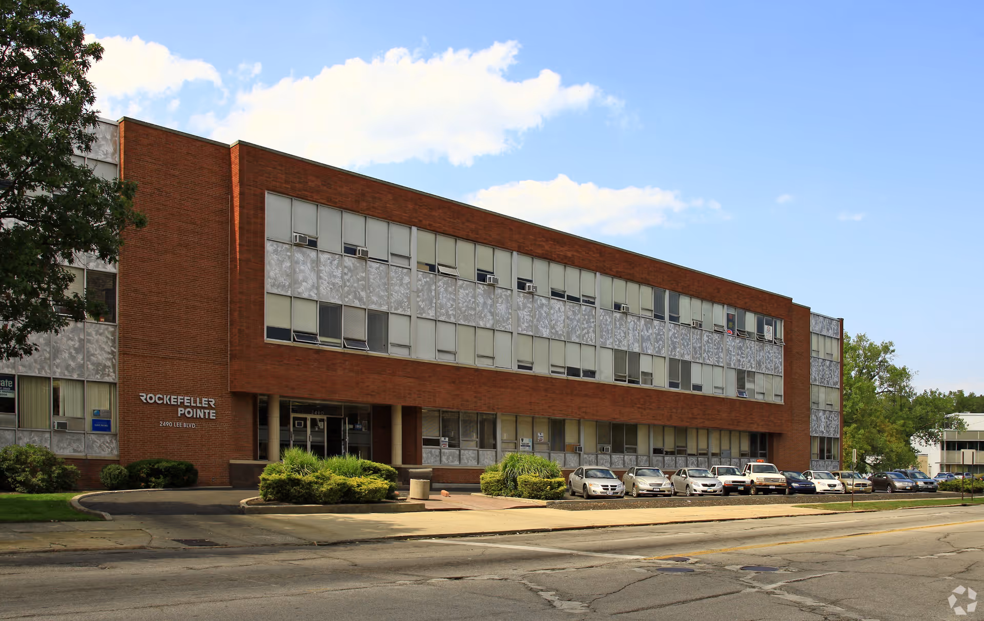 Exterior view of a brick senior living facility with a row of parked cars.