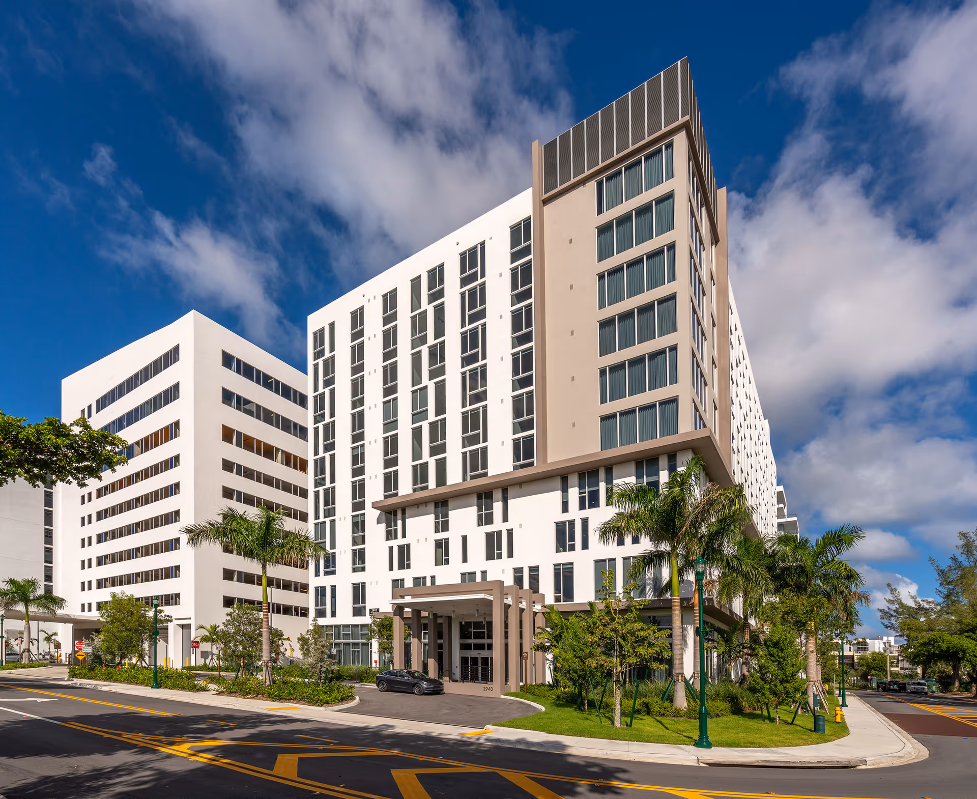 Modern multi-story senior living building with palm trees and a glass entrance.