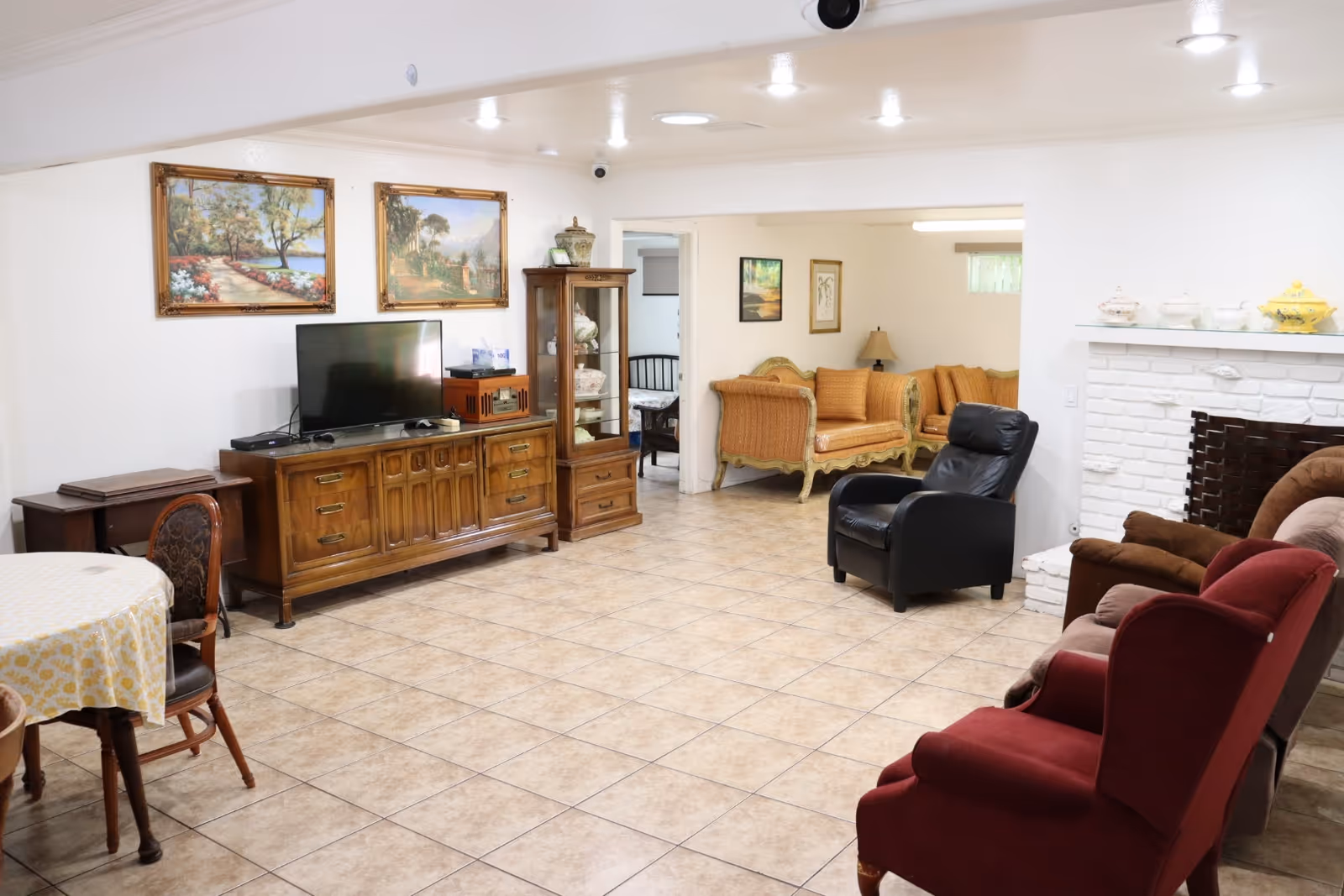 Cozy common room with TV, seating, round table, and fireplace in a senior living facility.