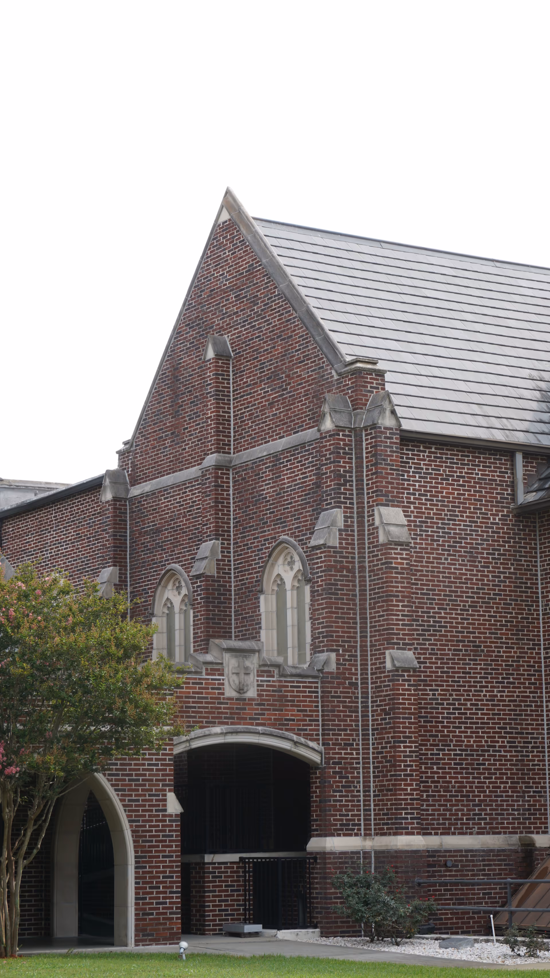 Brick Gothic-style building with arched windows, peaked roof, and surrounding trees.