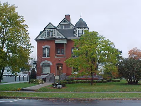 Red brick Victorian-style building with a turret, set among trees and a manicured lawn.