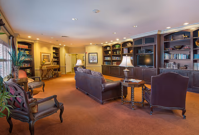 Comfortable lounge with leather sofas and armchairs, side tables and lamps, and built-in bookshelves lining the back wall.