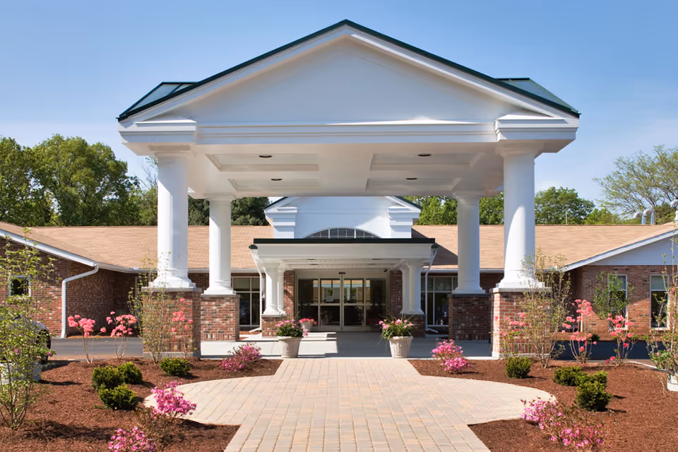 Front entrance of Kent Regency with a covered portico supported by white columns, brick facade, and a landscaped walkway.