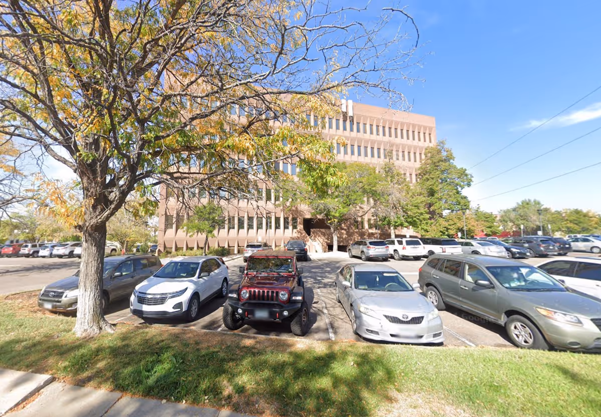 Exterior view of a multi-story brick building with a parking lot and trees.