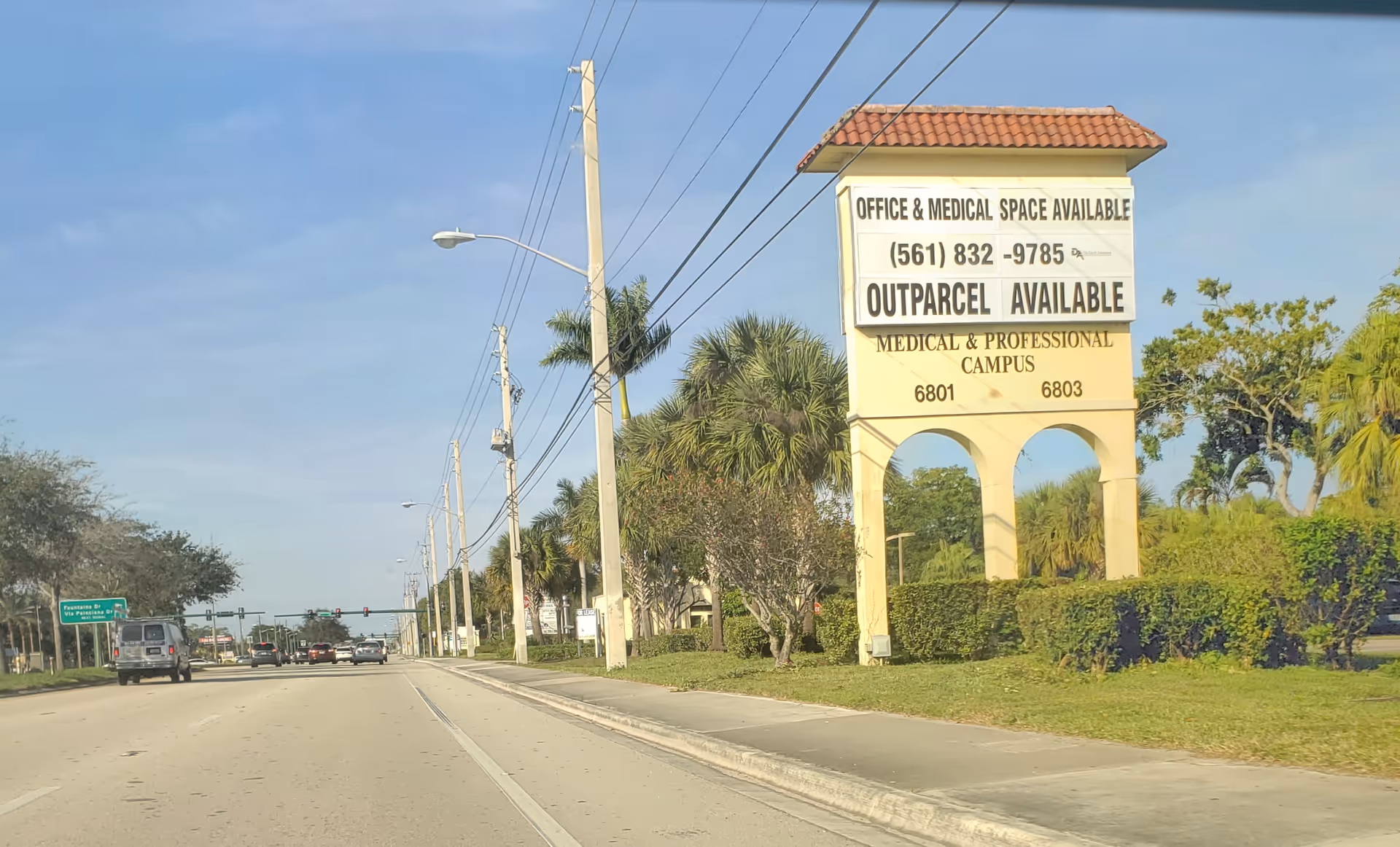 Tall beige sign advertising office and medical space on a palm-lined street.