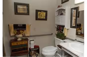 Compact bathroom with toilet, sink, mirror, and accessibility grab bar in a senior living facility.