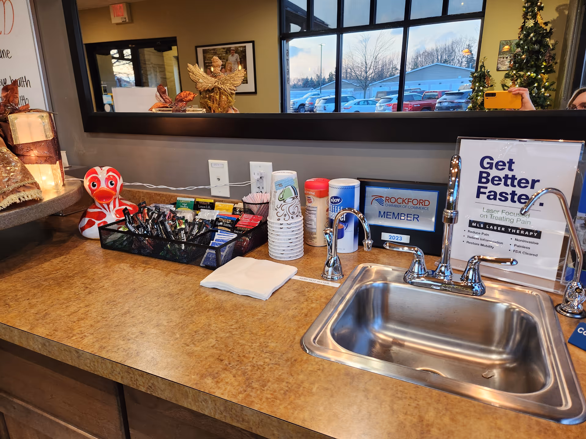 A stainless sink and beverage station along a brown counter inside a facility lobby.