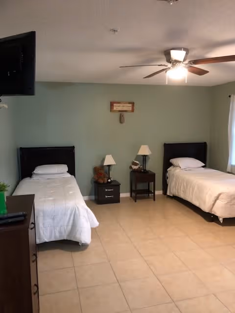 Spacious bedroom with two twin beds, nightstands, lamps, a ceiling fan, and tiled floor.